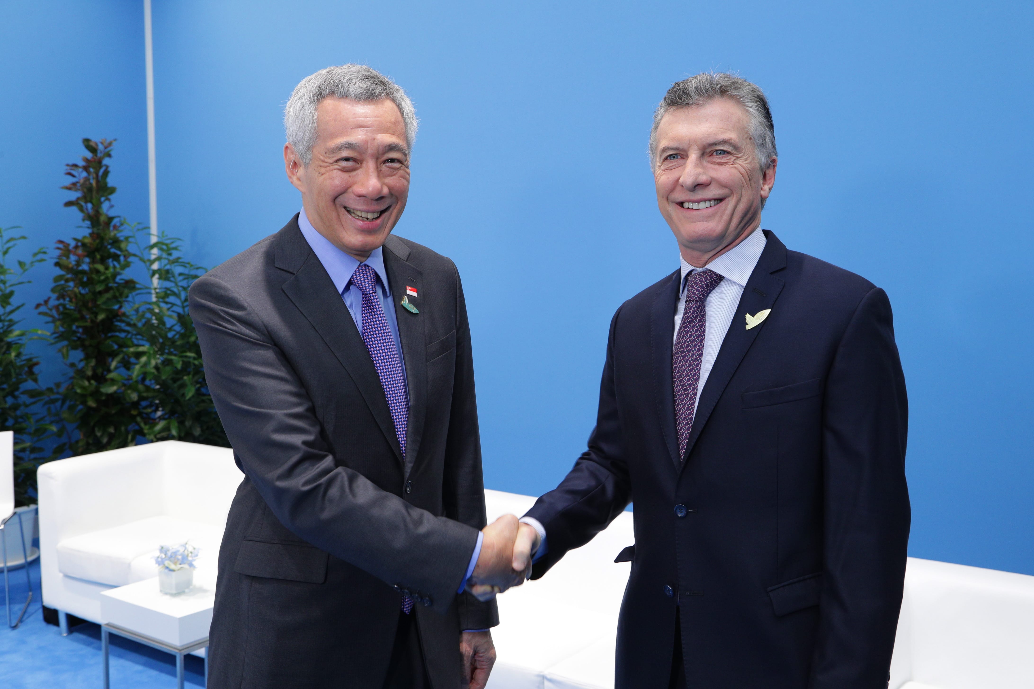 Lee Hsien Loong and Mauricio Macri shake hands in suits against a blue backdrop.