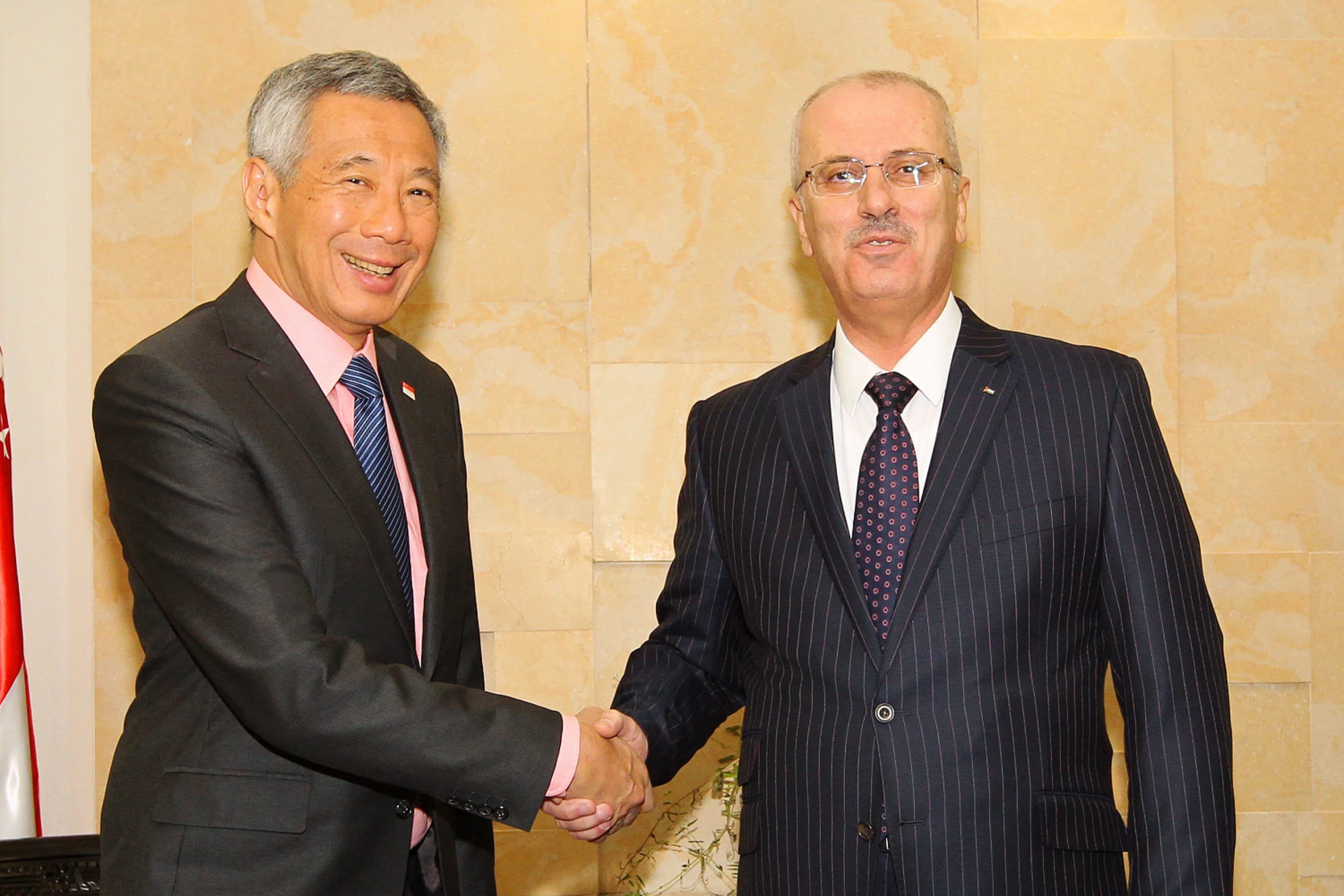Lee Hsien Loong and Mahmoud Abbas shake hands in suits before a marbled wall.