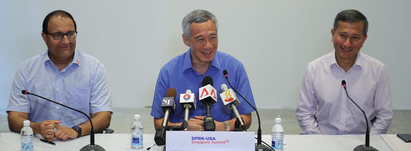 Three men at a press conference with microphones labeled "DPRK-USA Singapore Summit".