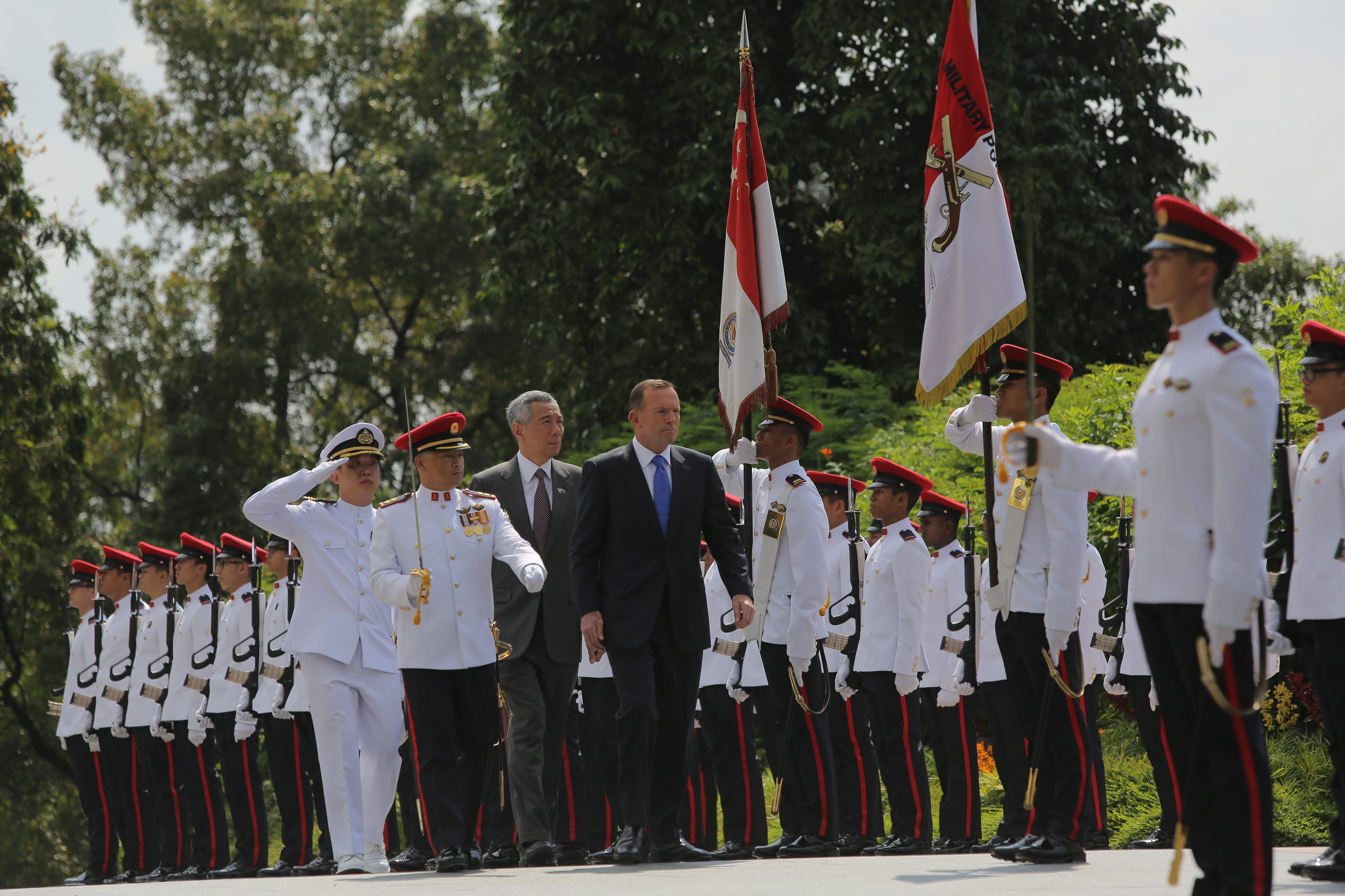 Military parade with uniformed soldiers, Singapore flag, and man in a suit.