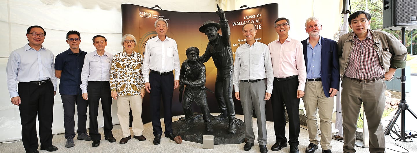 Nine people stand in front of a Wallace and Ali sculpture, with NUS signage in the background.