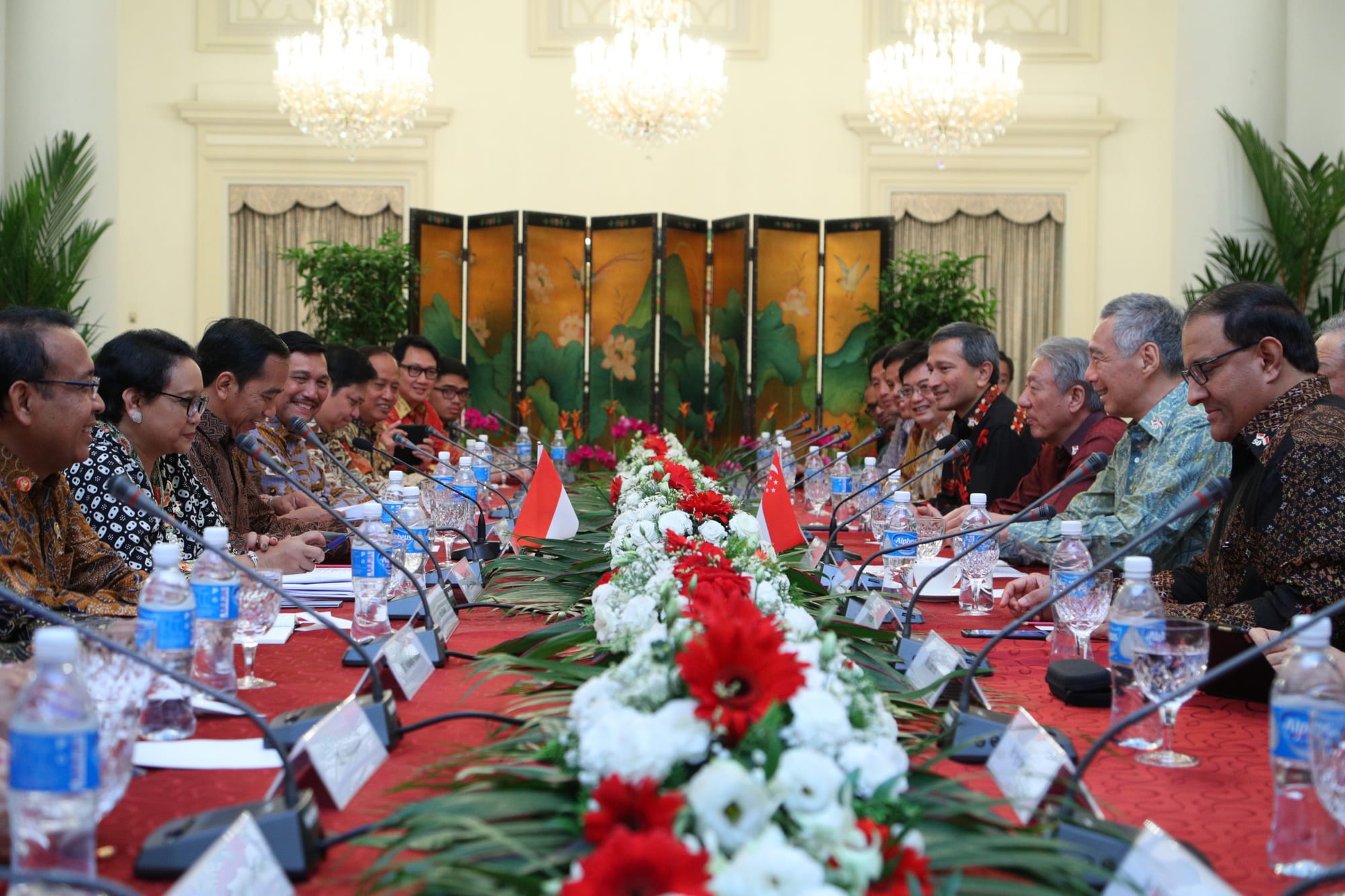 People seated at long table with flower centerpiece, Indonesian and Singaporean flags visible.