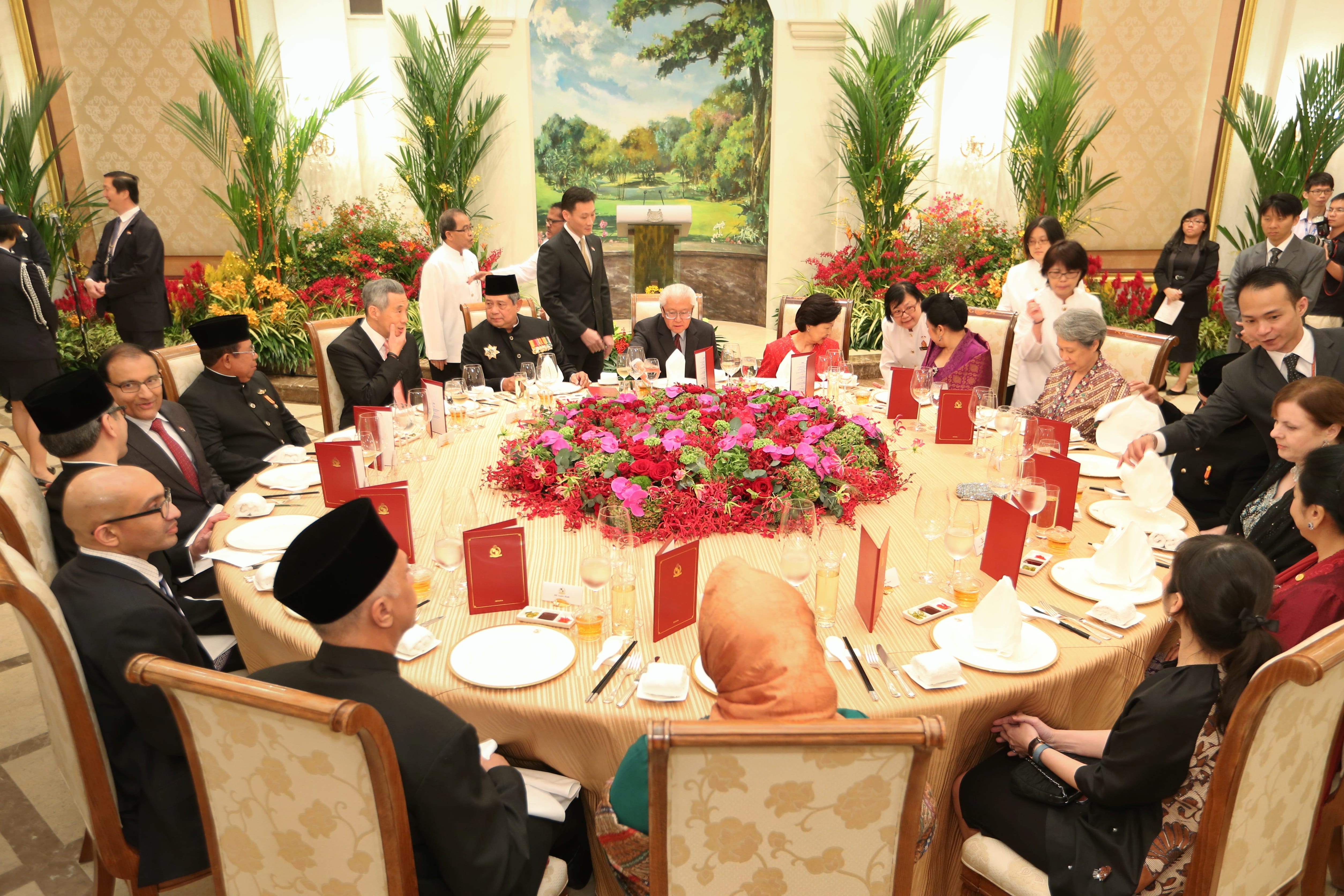 People seated around a round table with formal place settings and large floral centerpiece.