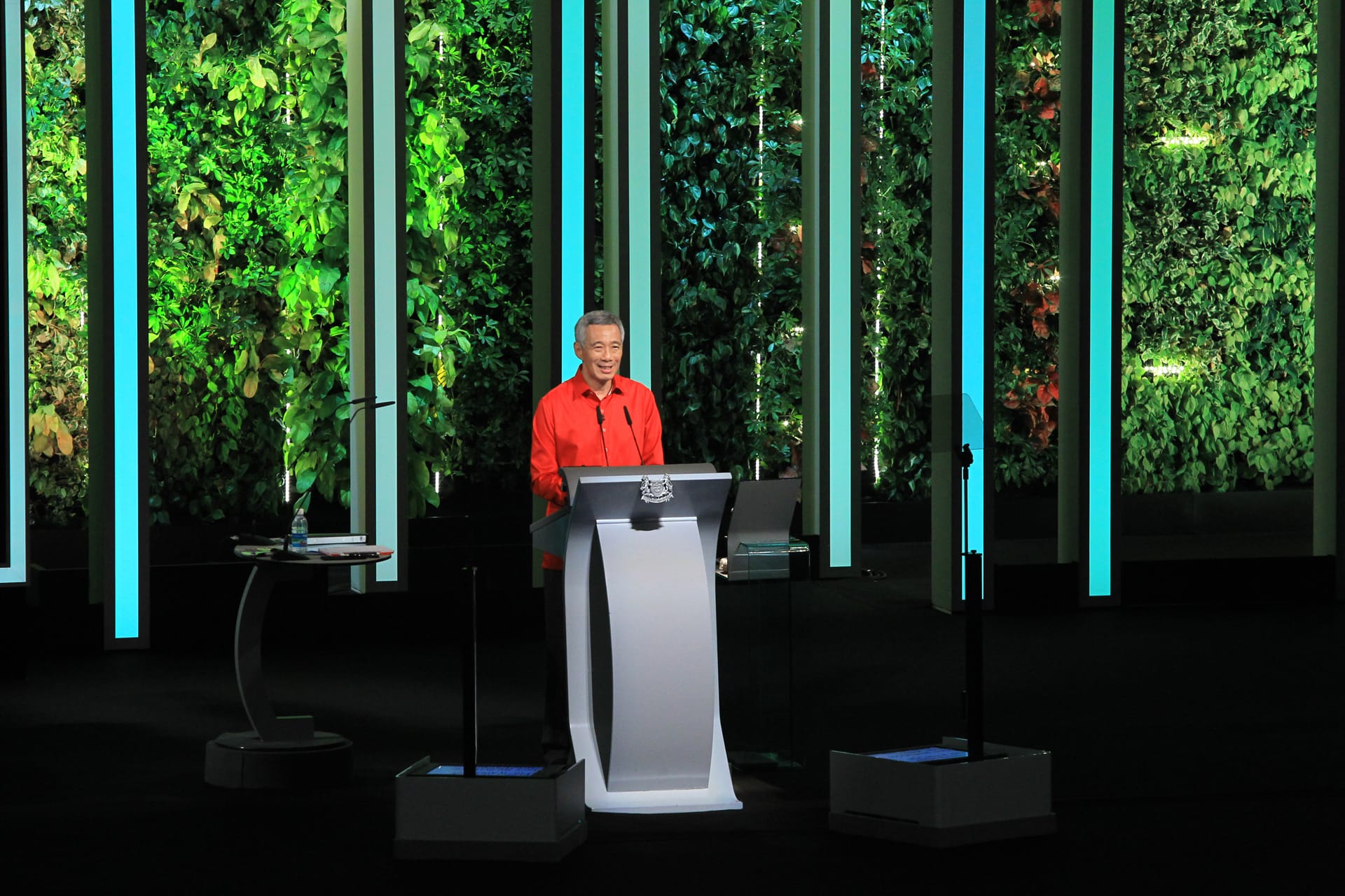 Lee Hsien Loong at podium with vertical gardens & blue lights in background.