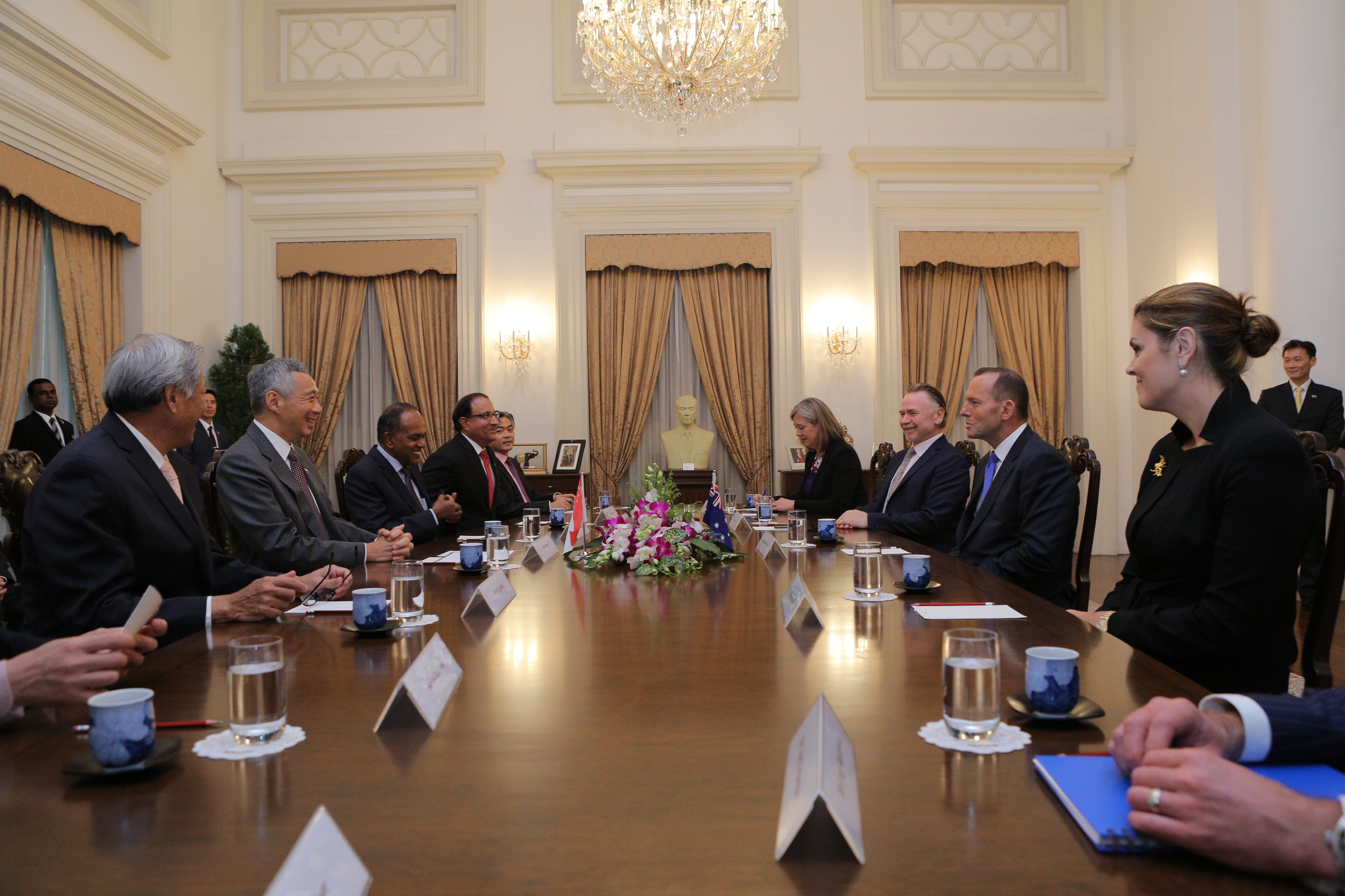 People seated around a long wooden table with flags and floral arrangement.