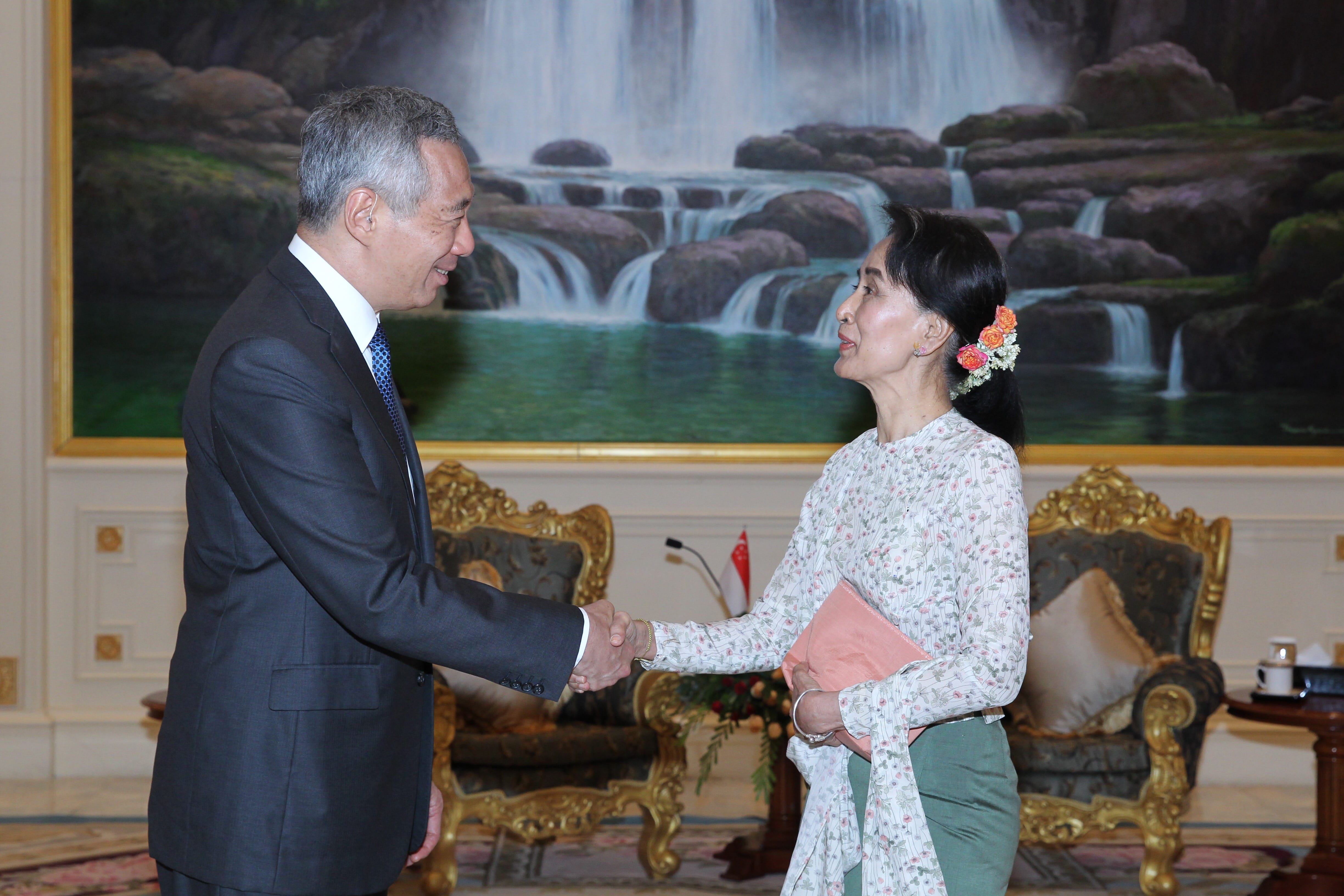 Lee Hsien Loong and Aung San Suu Kyi shake hands before a waterfall painting.
