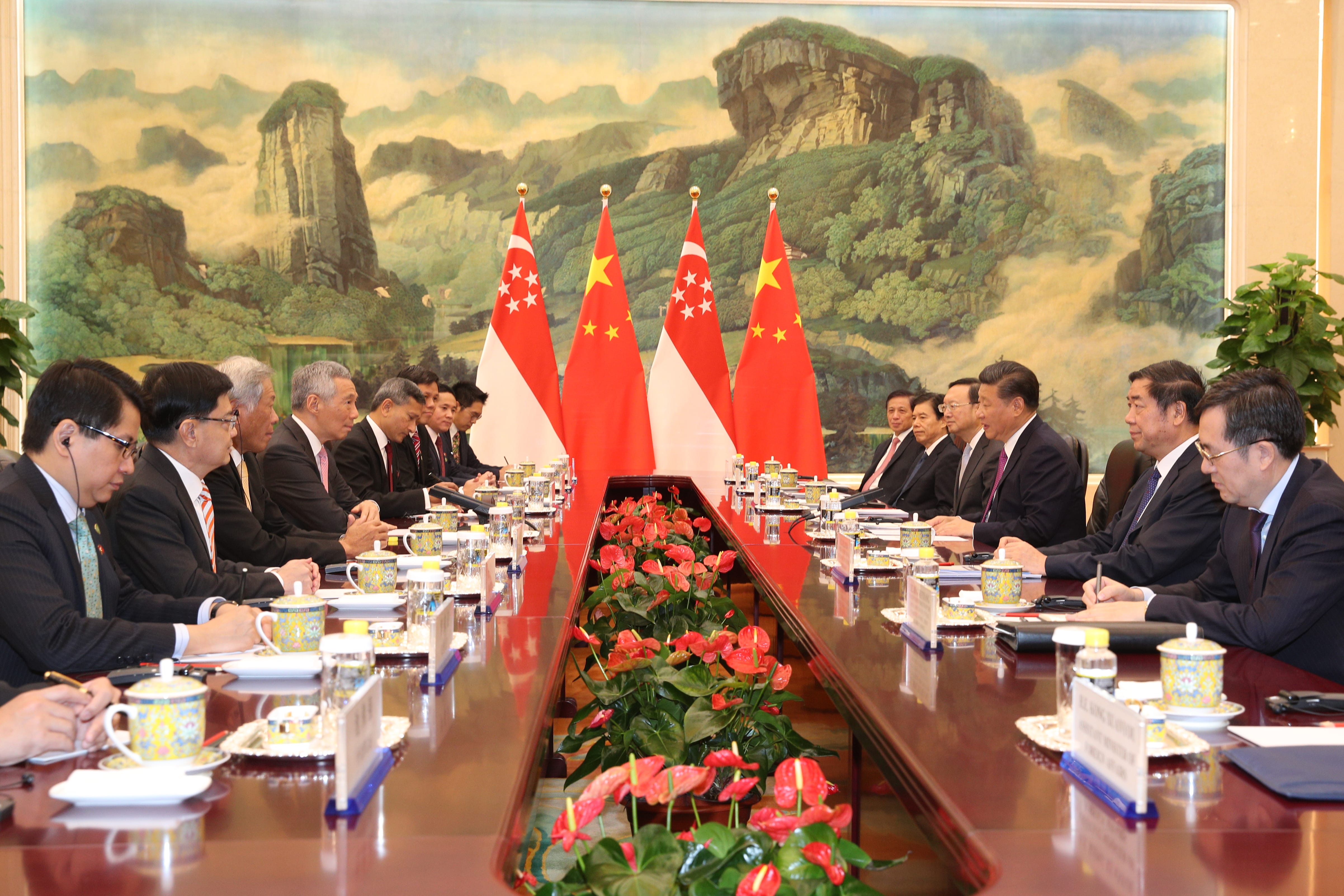 People at a long table with flags of Singapore and China, plus red flowers.