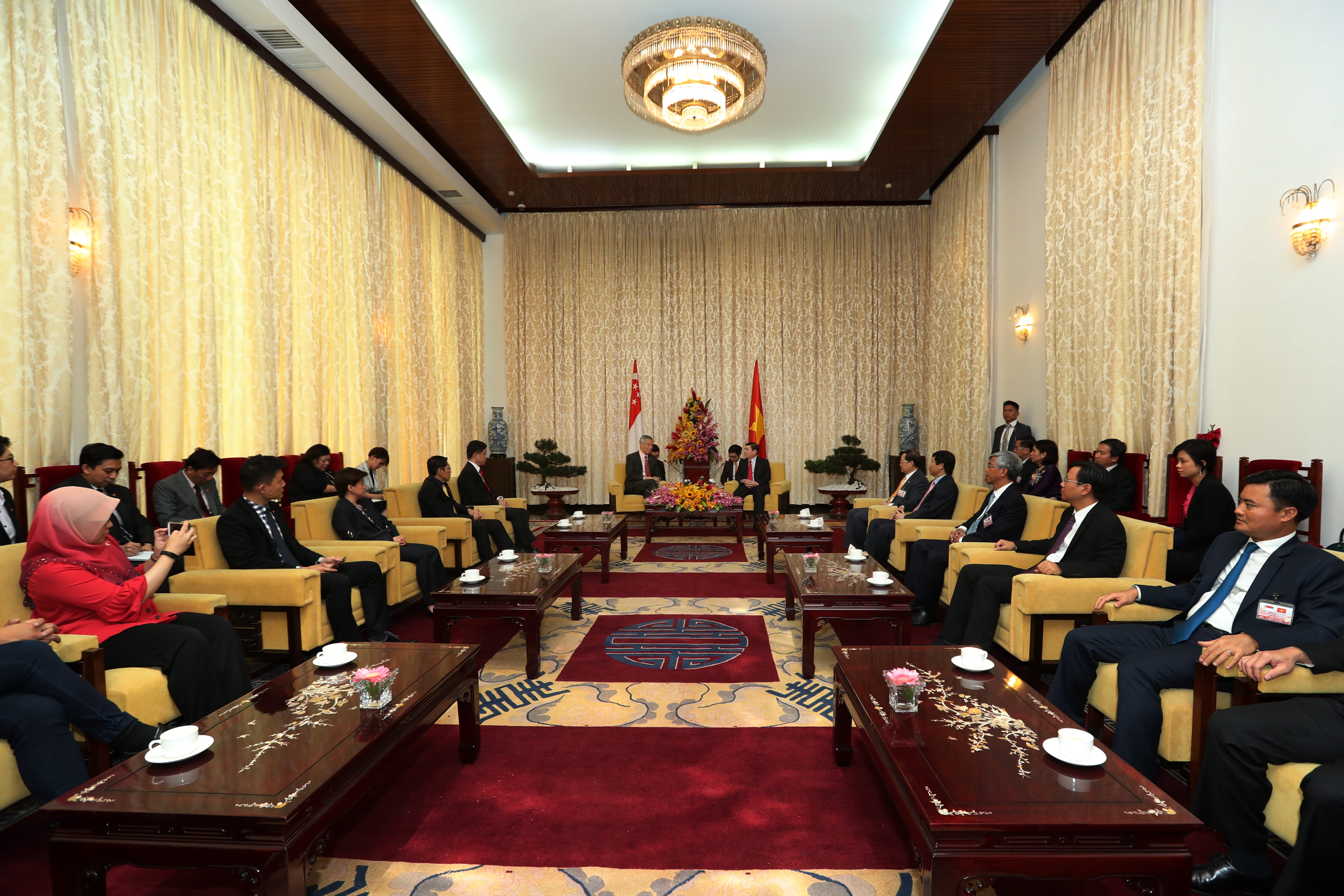 Meeting room with seated delegates, Singapore and Vietnam flags, decorative chandelier.