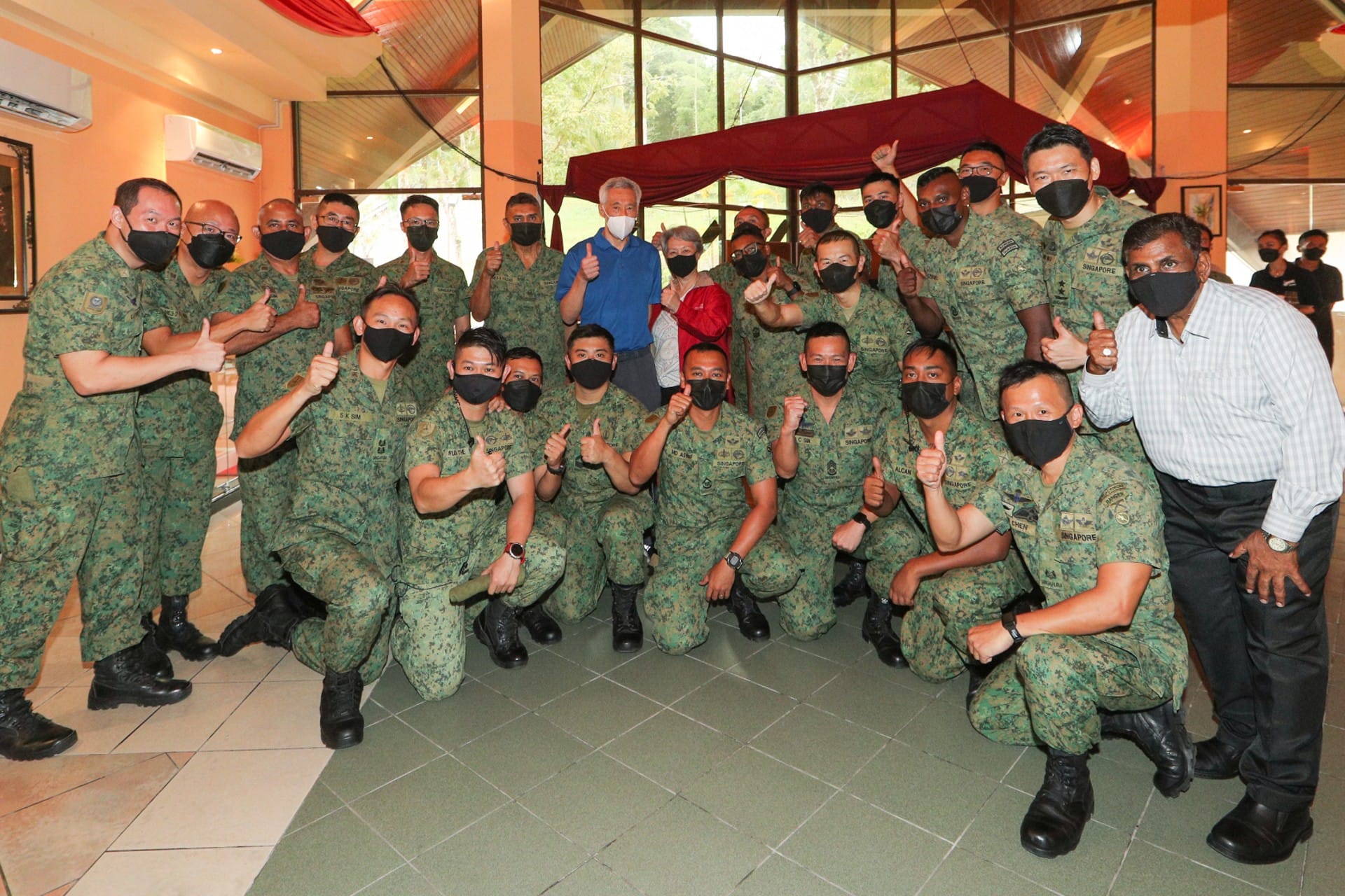 Group of people wearing Singapore military uniforms and face masks giving thumbs up.