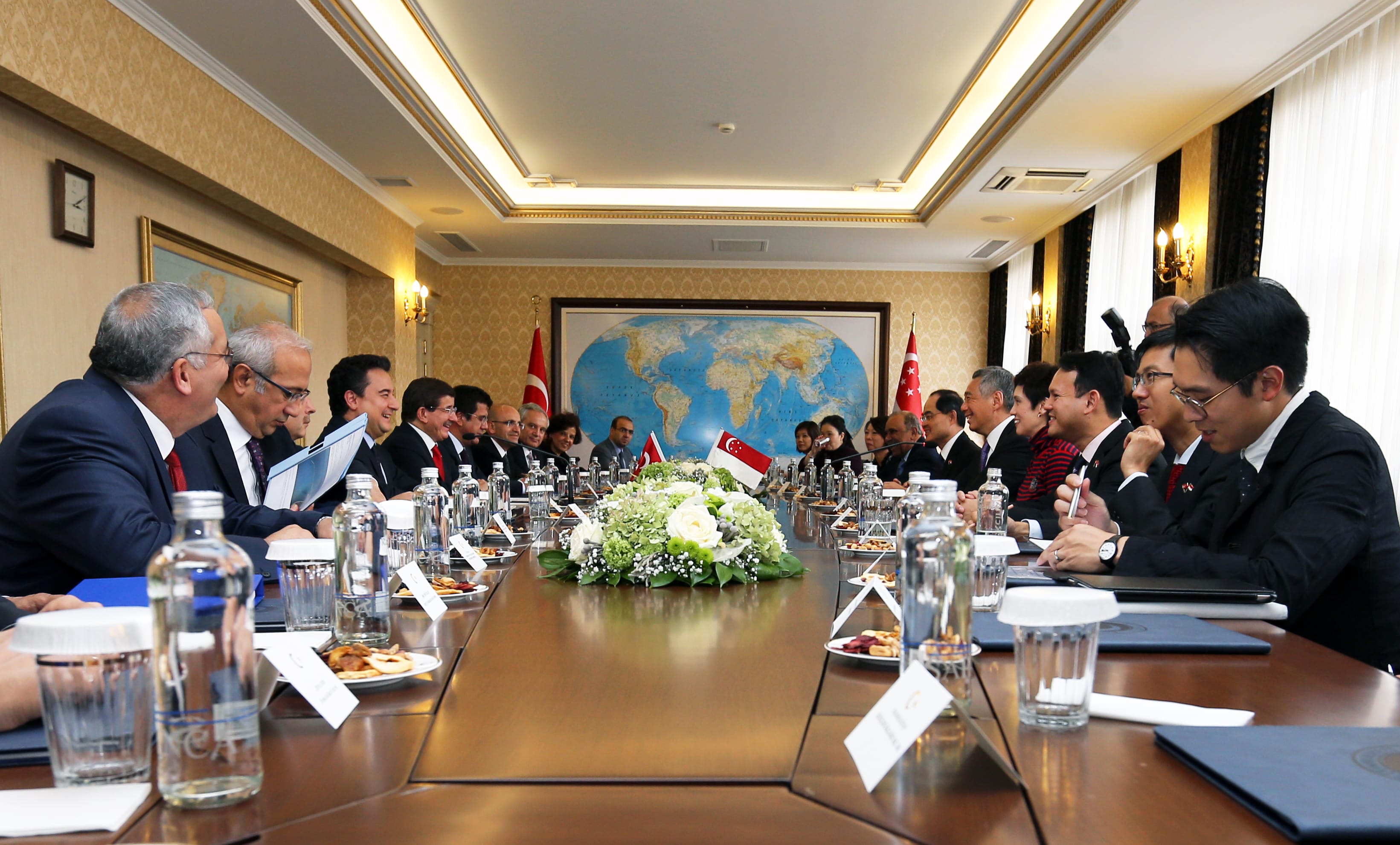 People at a long conference table. Water bottles, flags, and food. World map in background.