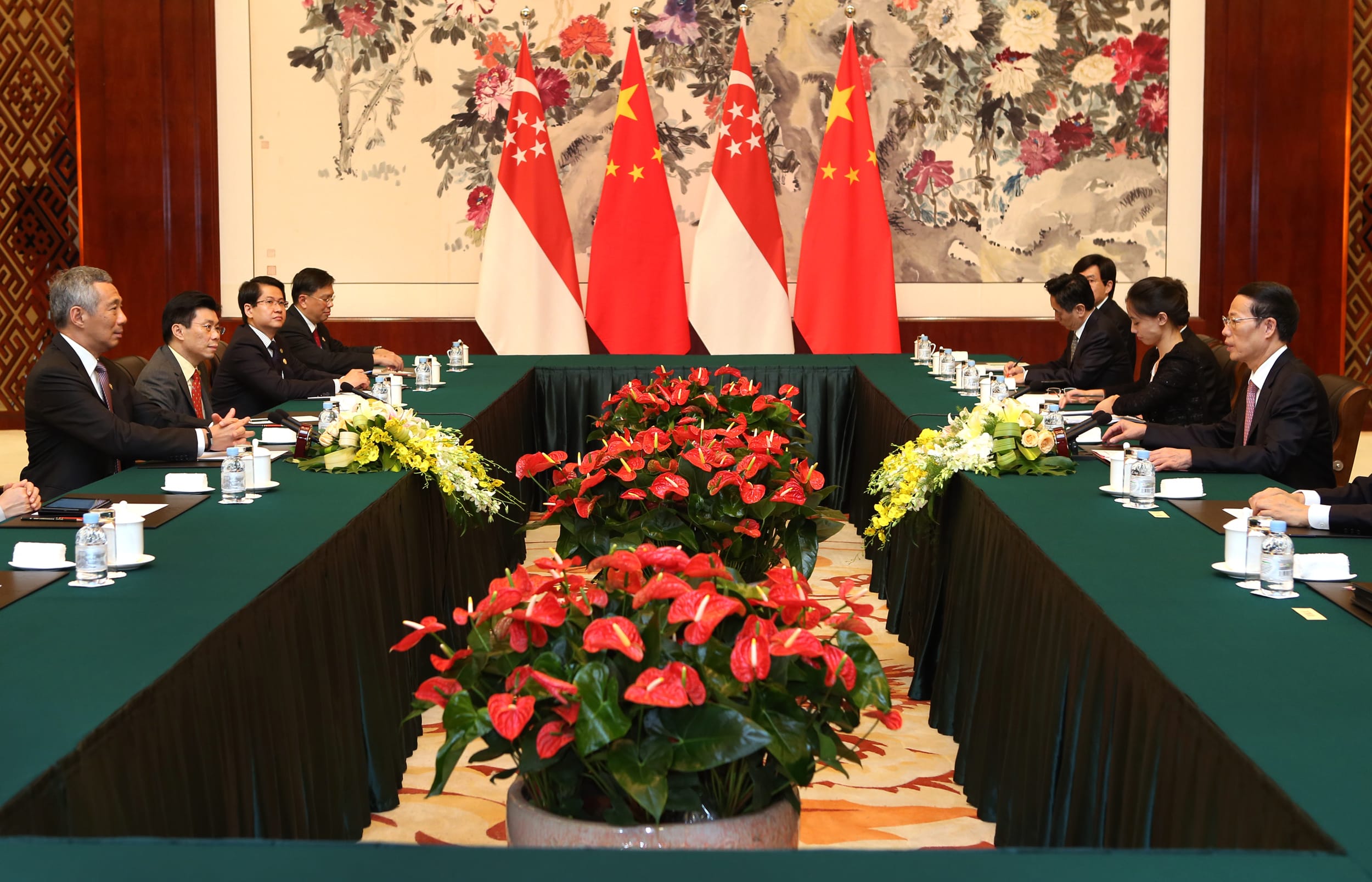 People seated at a long green table with flags of China and Singapore in the background.