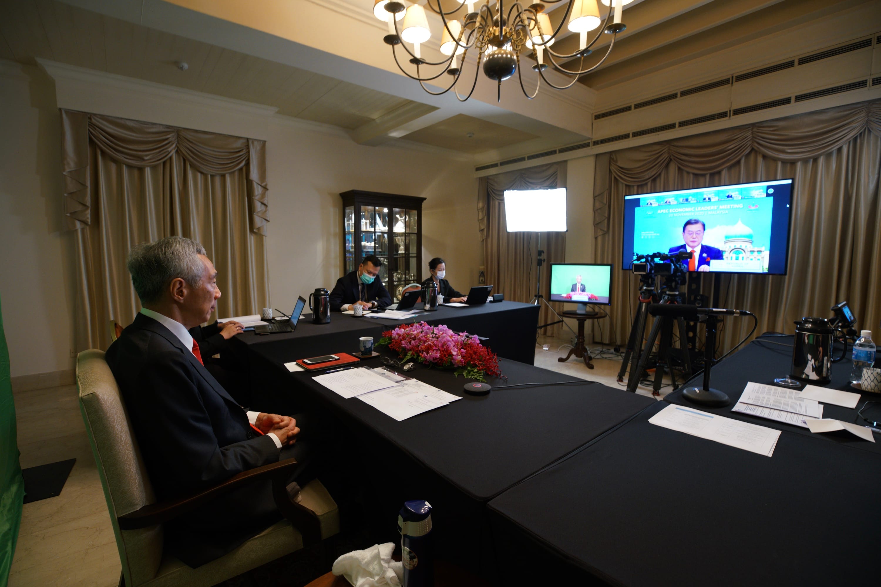 Lee Hsien Loong at a virtual APEC meeting, with staff in masks. Monitors and cameras present.