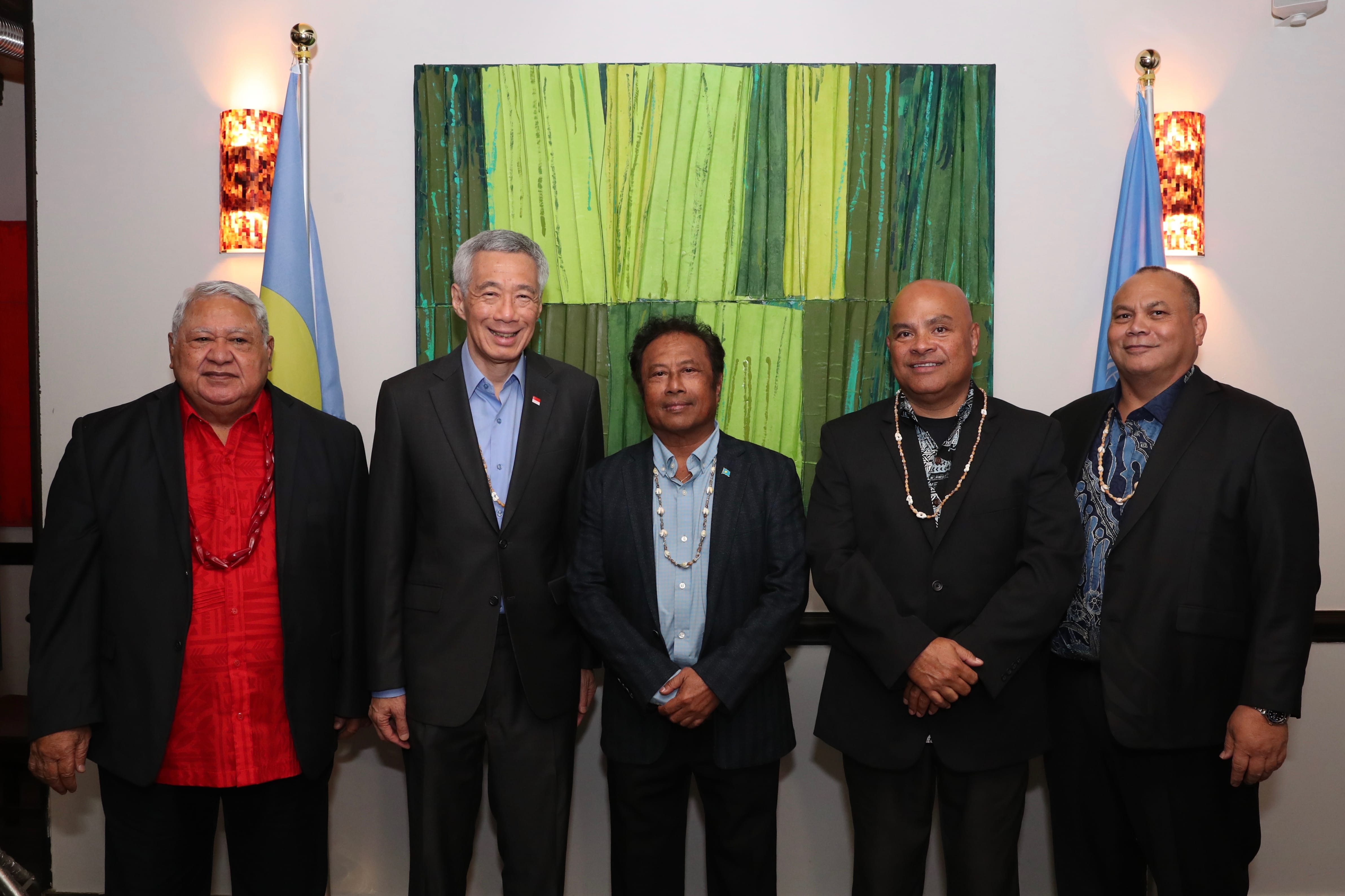 Five men in suits pose before flags and a green abstract painting. Lee Hsien Loong is in the center.
