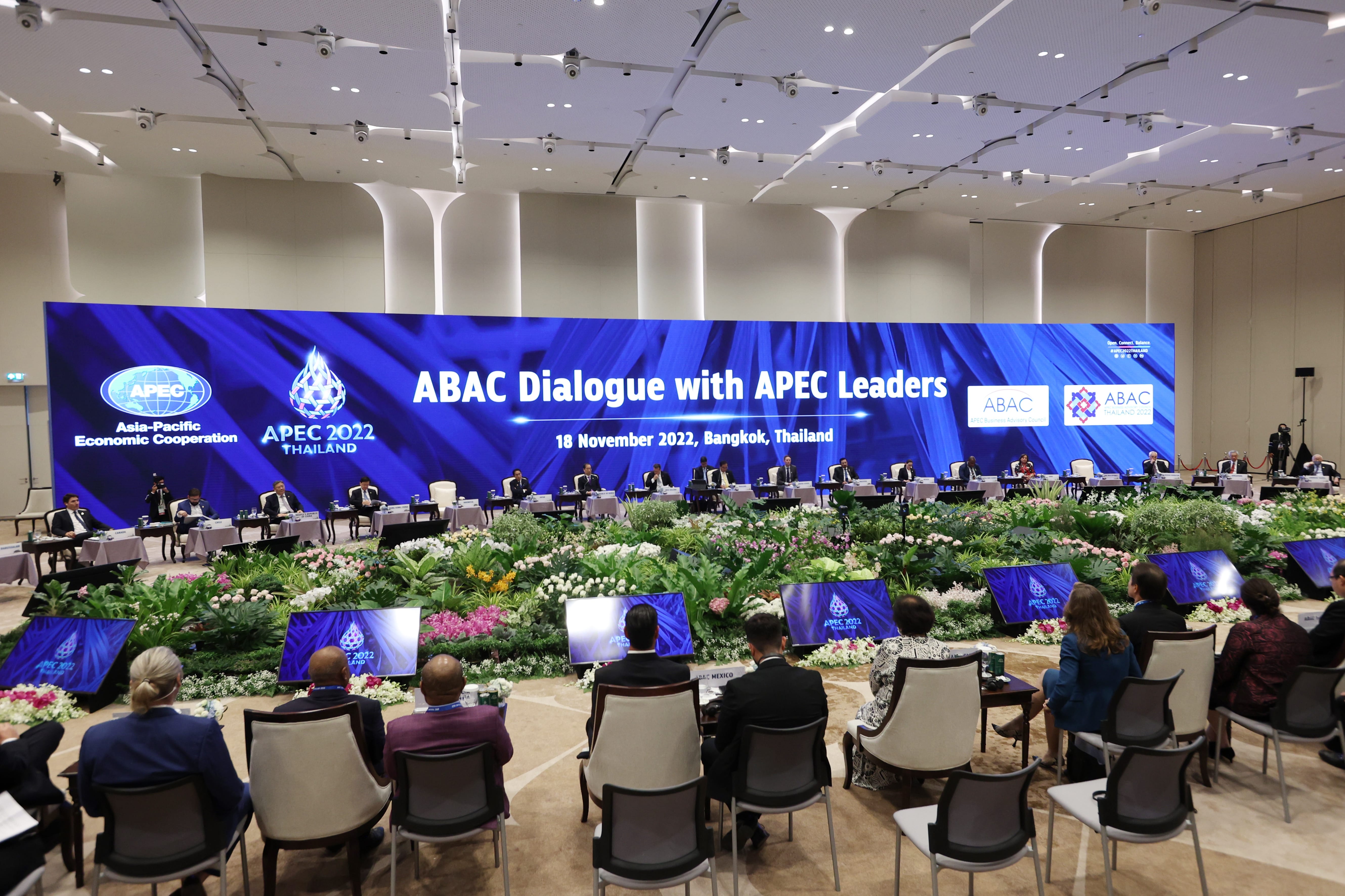 APEC 2022 Thailand conference with speakers at tables amid floral arrangements, audience seating visible.