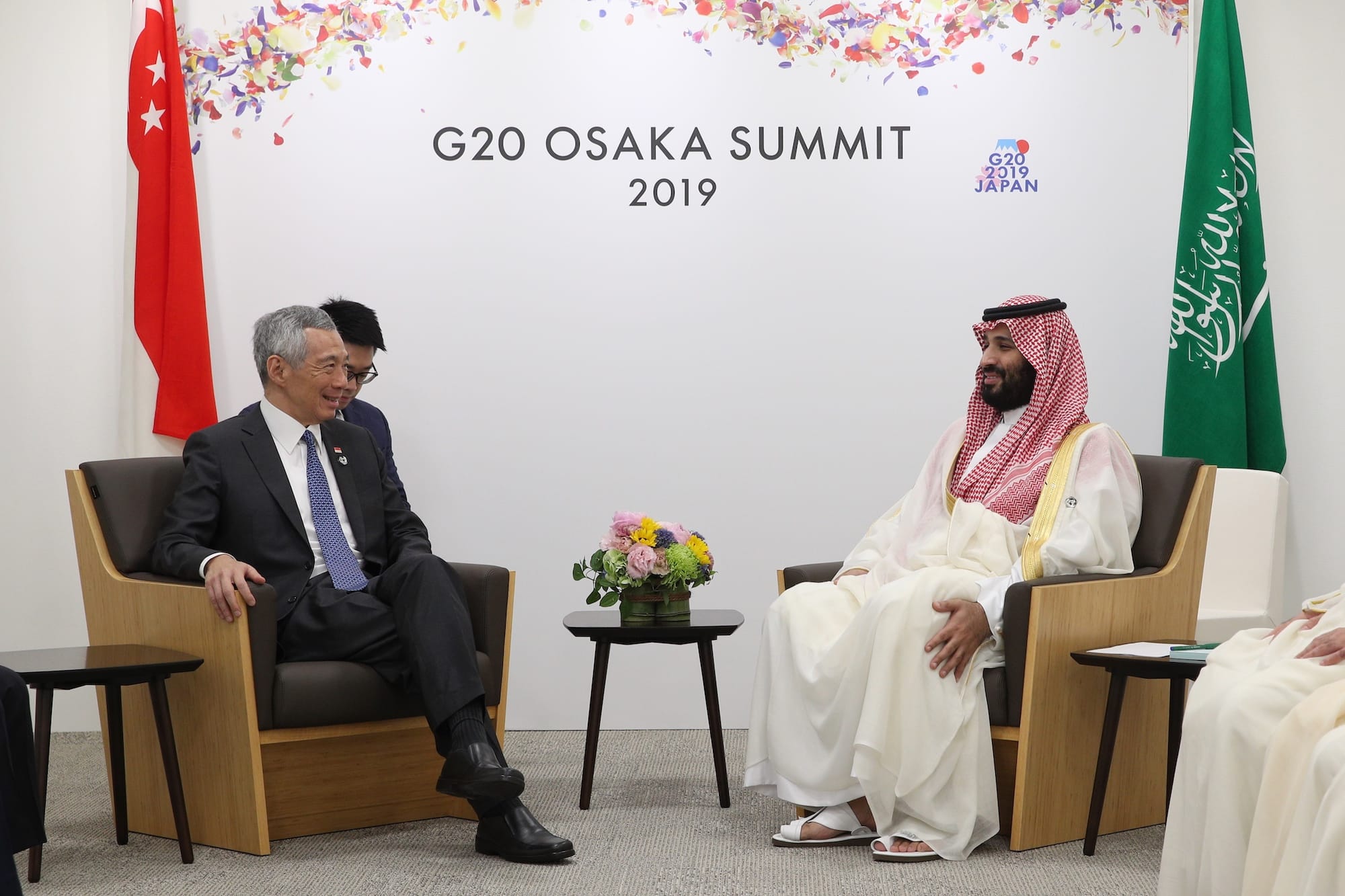 Two men sit facing each other at G20 Osaka Summit, with Singapore and Saudi flags.