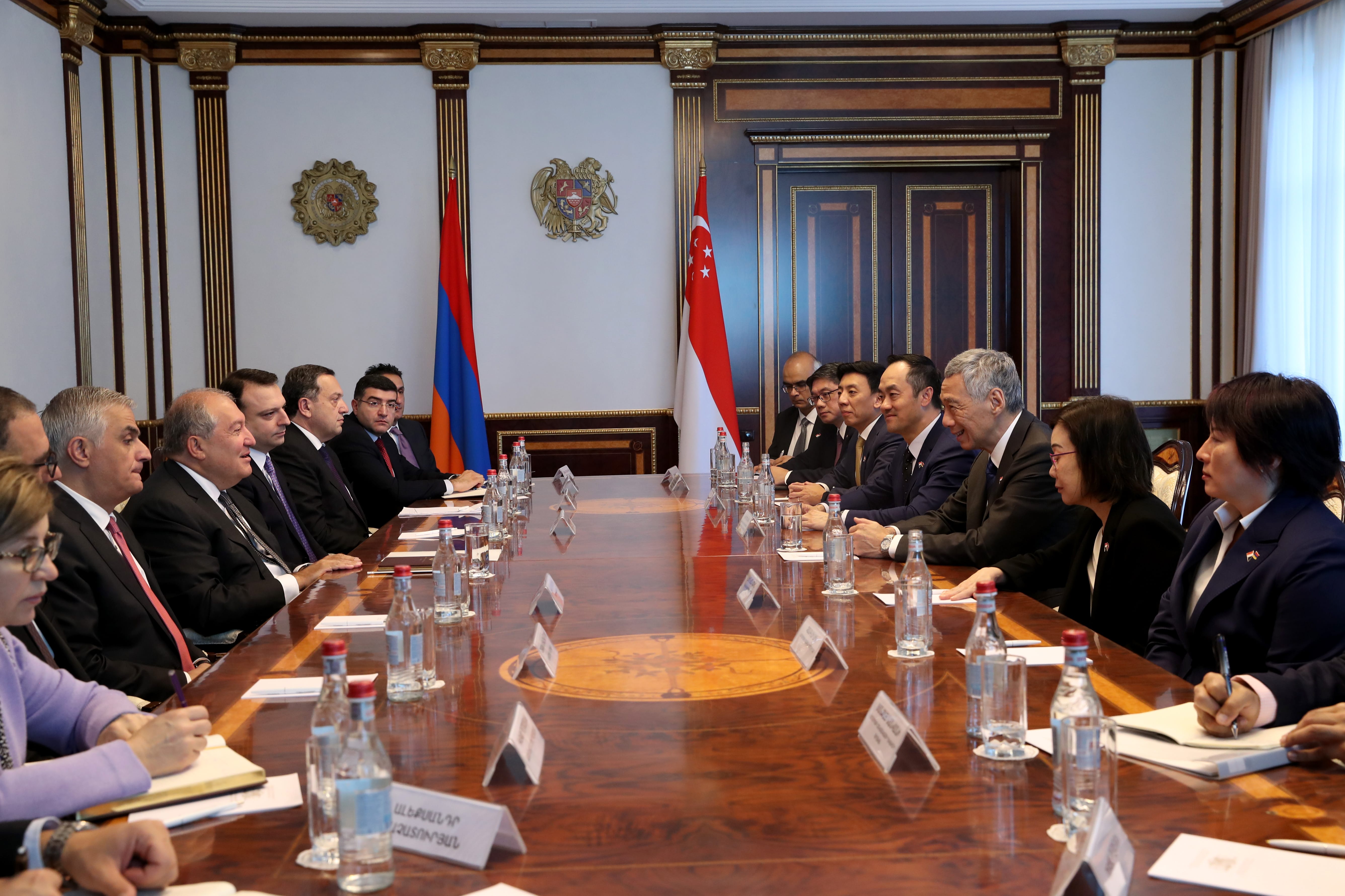 People at long table with flags of Armenia and Singapore, water bottles, and name cards.