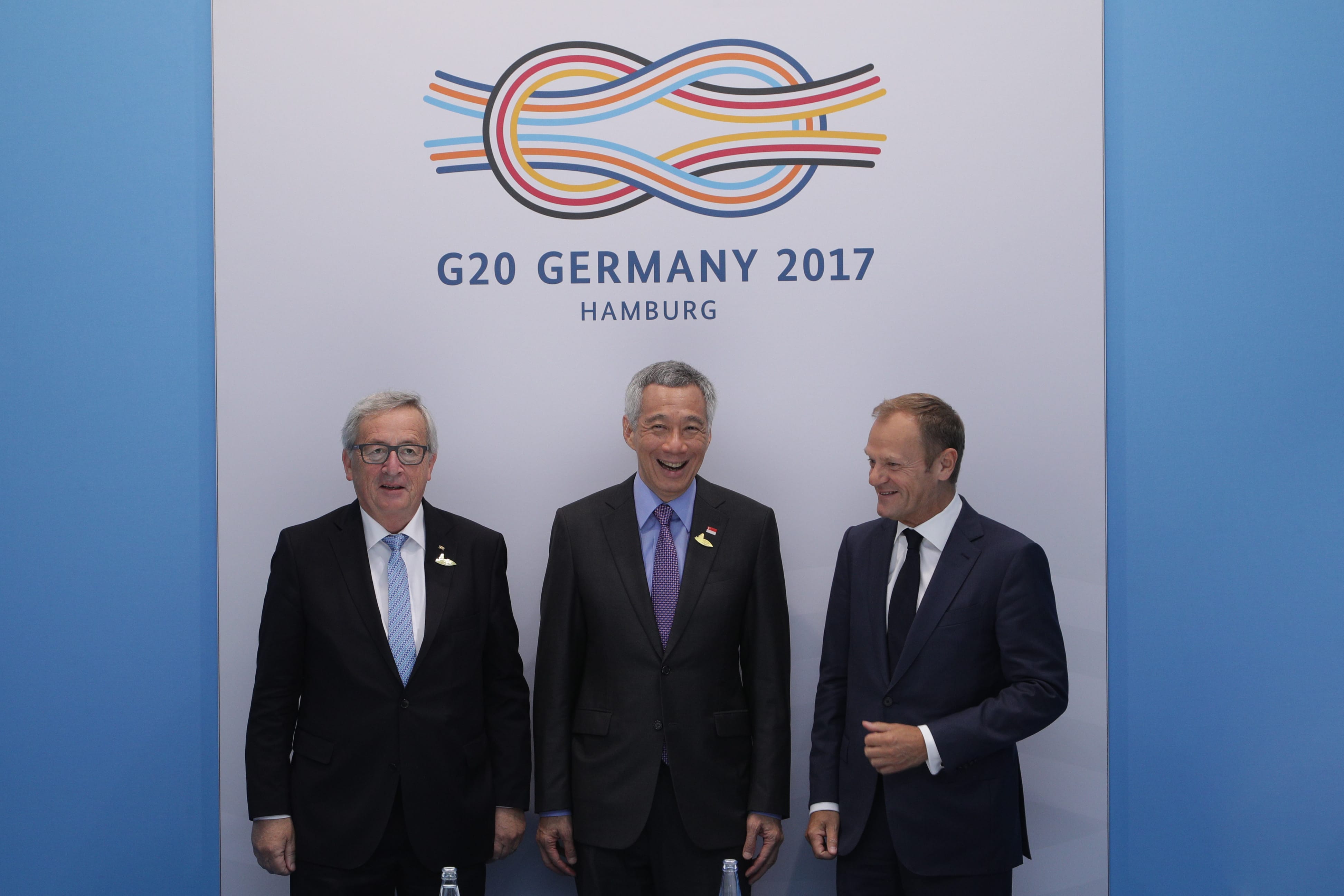 Three men in suits stand before a "G20 Germany 2017" logo.