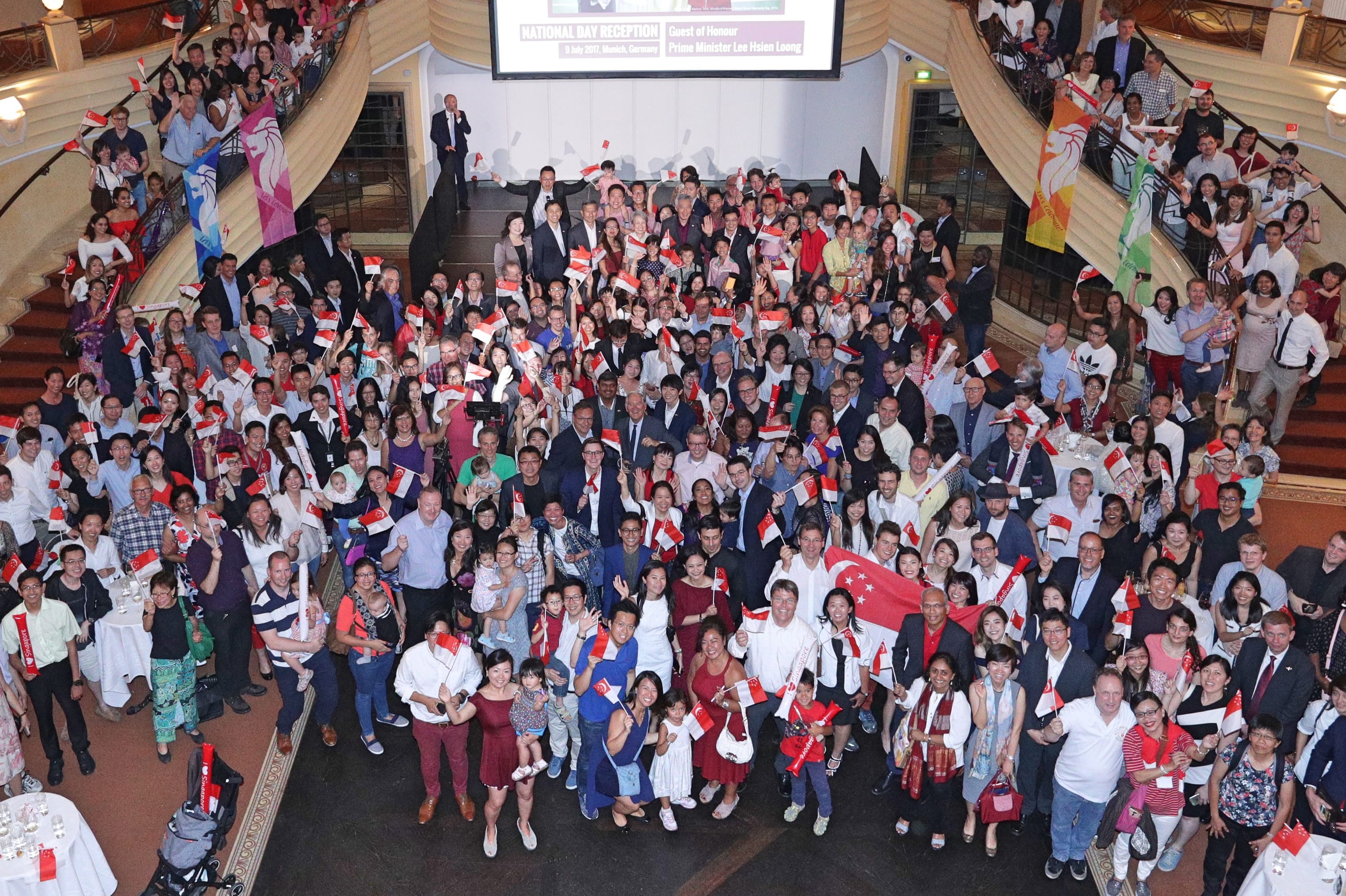 Large group of people hold Singapore flags and banners at a National Day Reception.