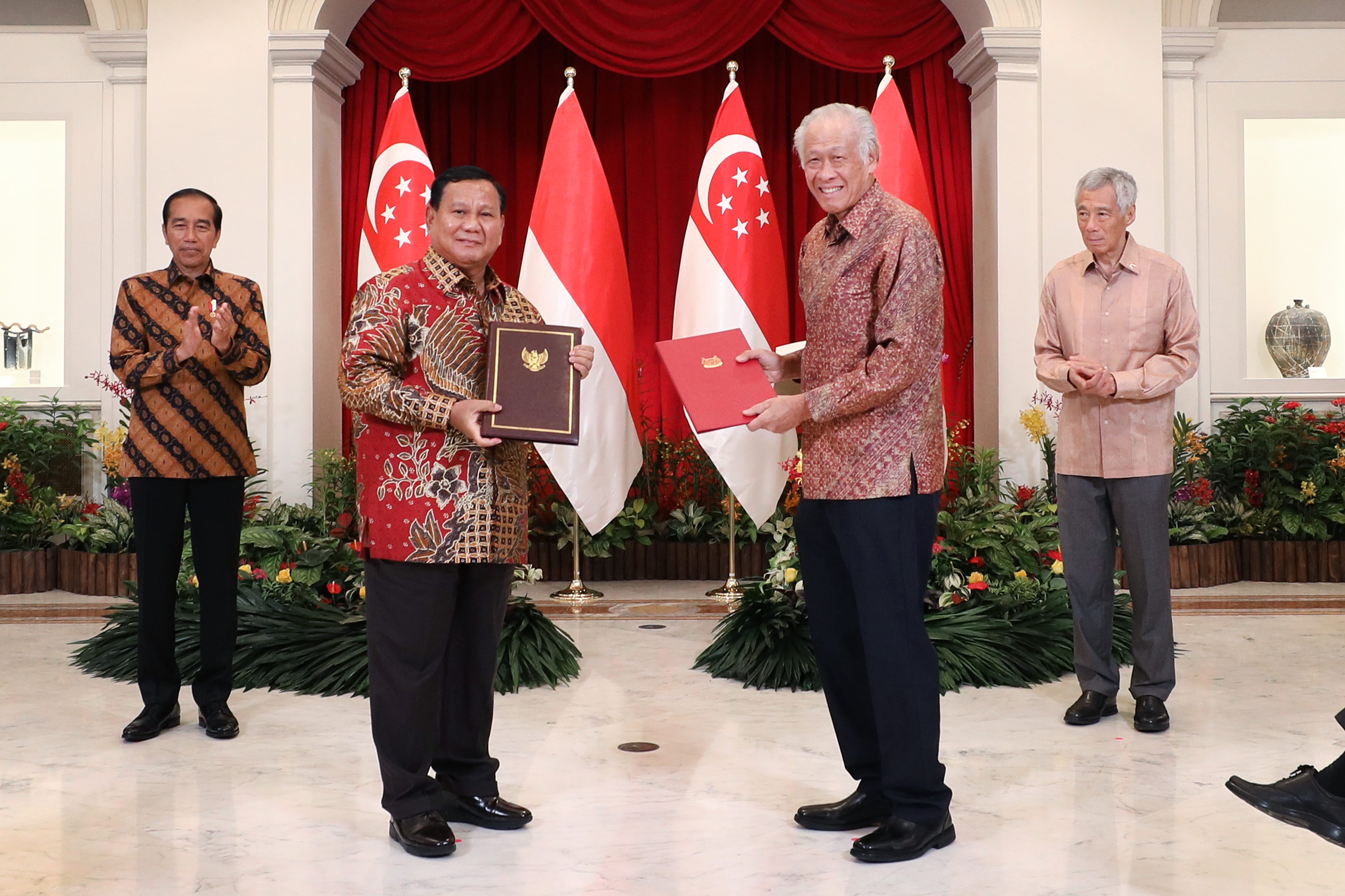 Four people in front of Singaporean and Indonesian flags are exchanging documents.