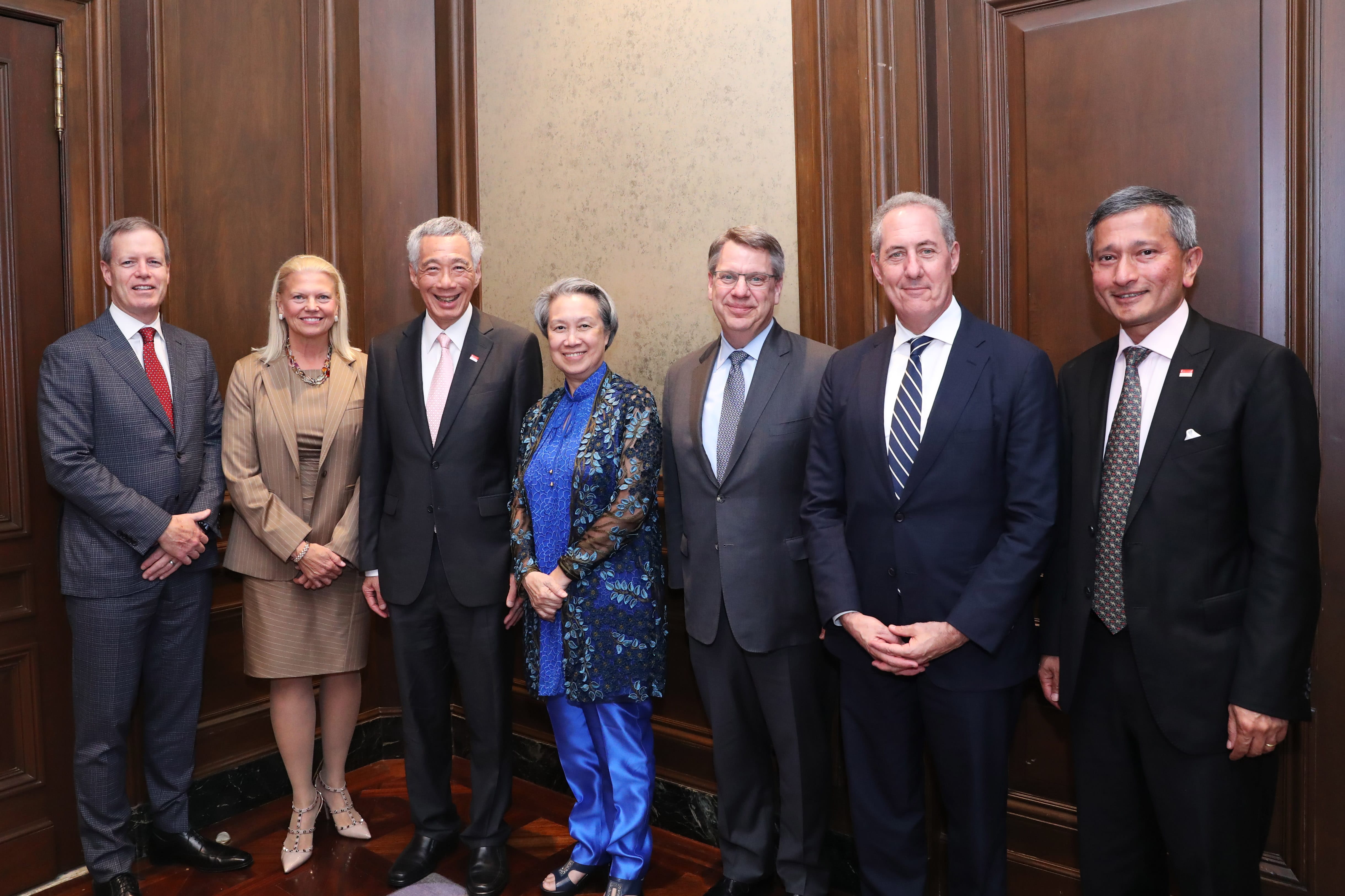 Group of people in business attire posing against wood-paneled wall. Lee Hsien Loong is visible.