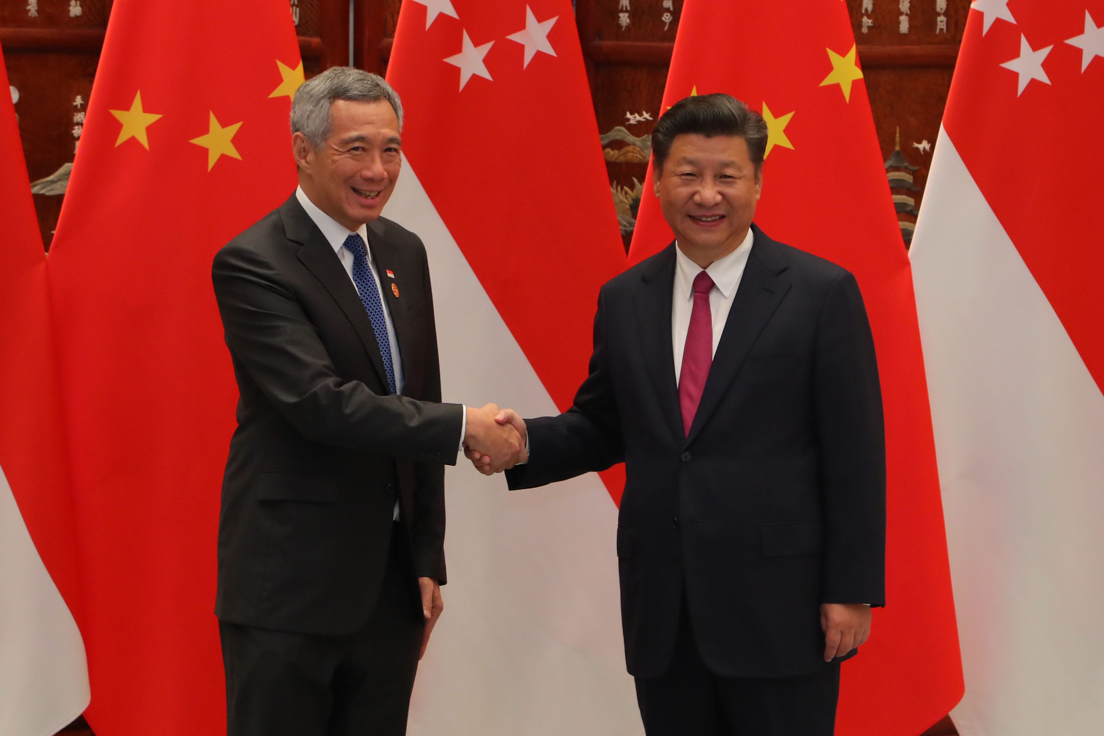 Lee Hsien Loong and Xi Jinping shake hands before Singapore and China flags.