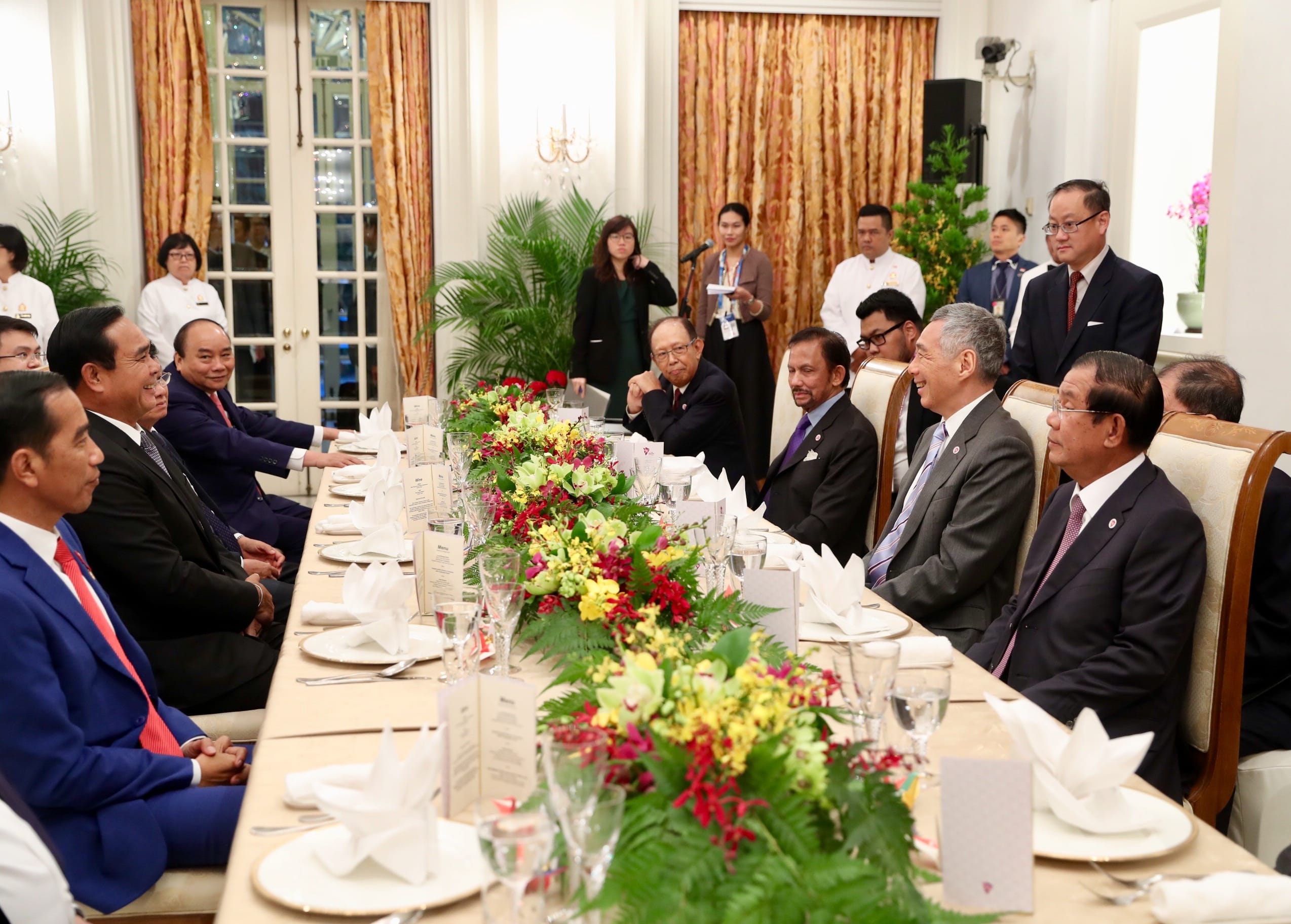 People seated at a long table with floral centerpieces, fine dining setup.