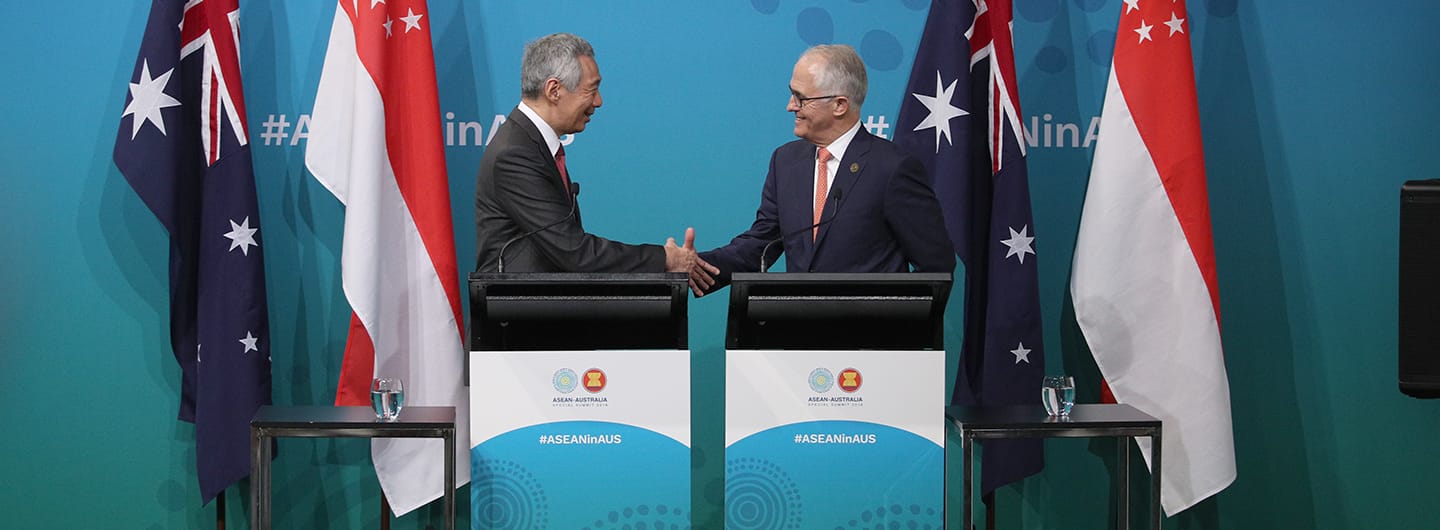 Lee Hsien Loong and Malcolm Turnbull shaking hands behind podiums with Australia and Singapore flags.