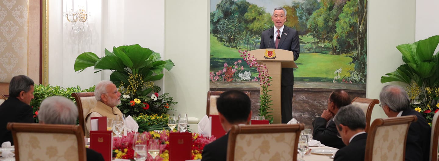 Lee Hsien Loong at podium addressing Narendra Modi and others seated at long dinner table.