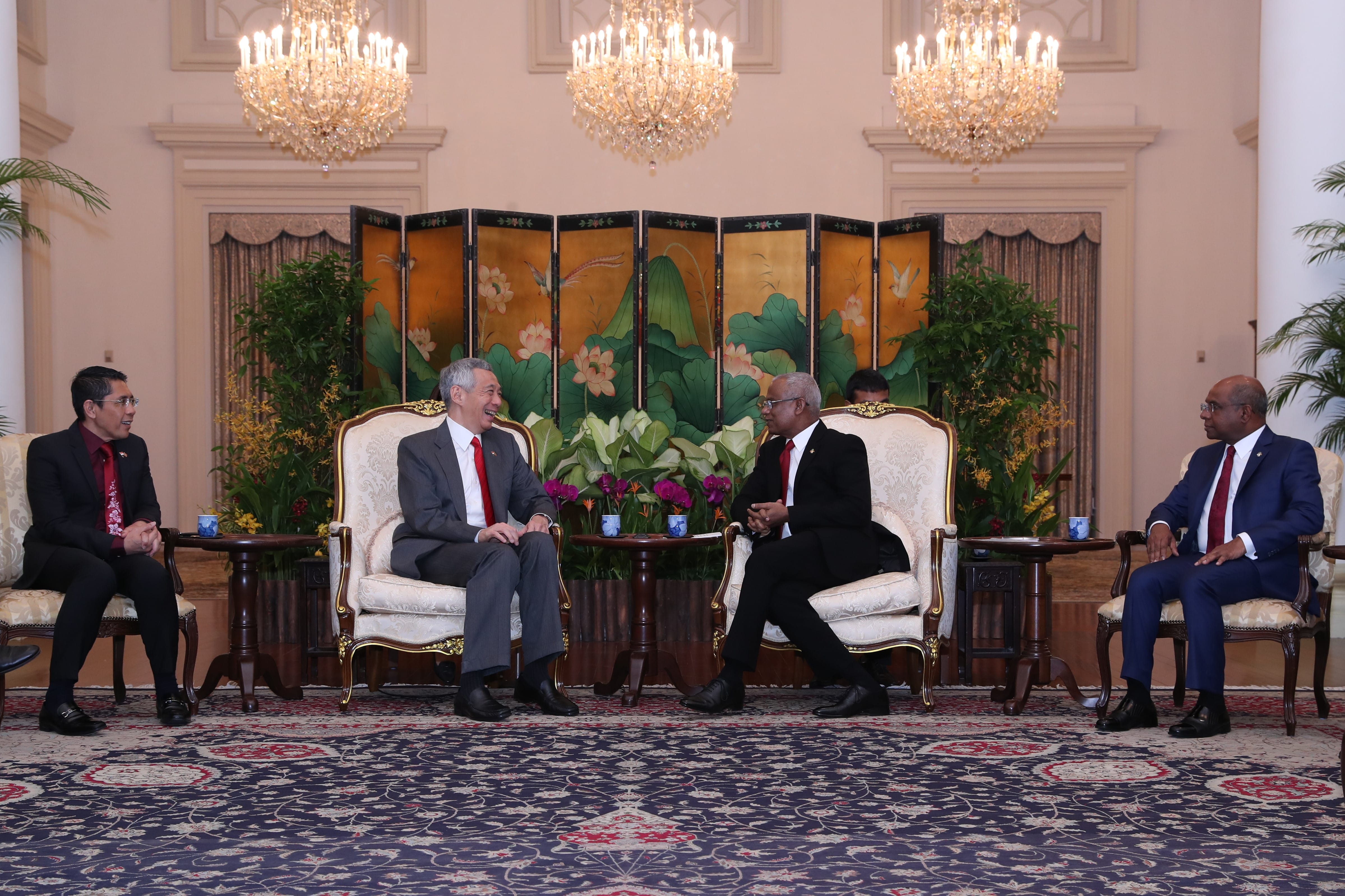 Two men in suits sit in ornate chairs, facing each other in an ornate room.