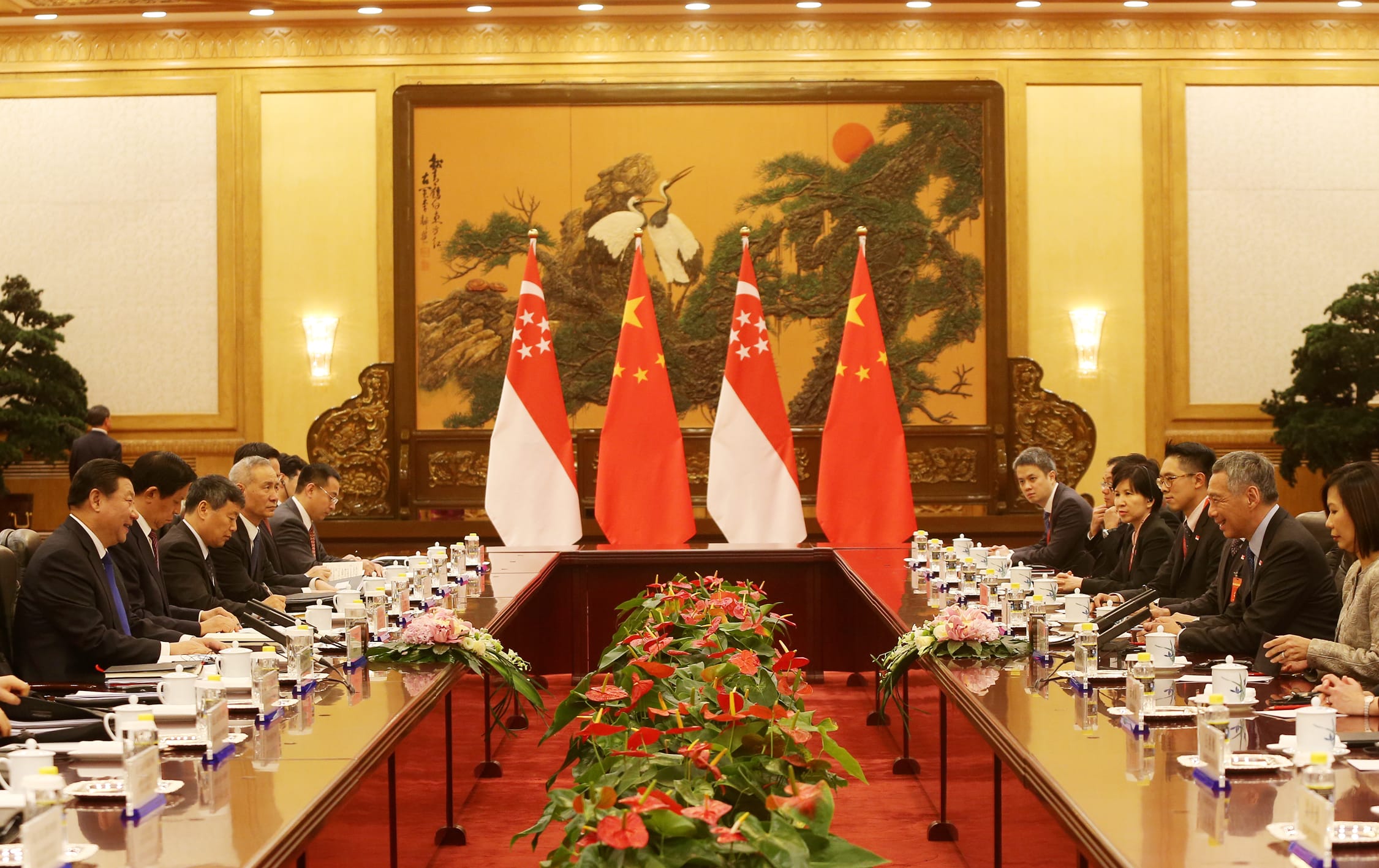Formal meeting with flag backdrops; delegates seated at a long table with floral arrangements.
