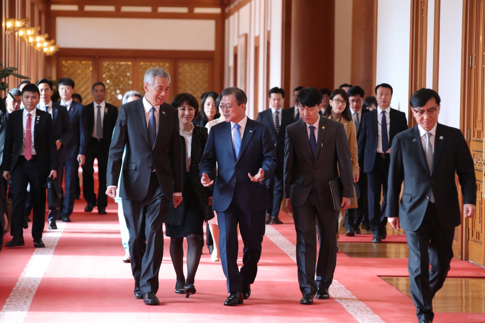 Lee Hsien Loong and Moon Jae-in walking on a red carpet with many people.