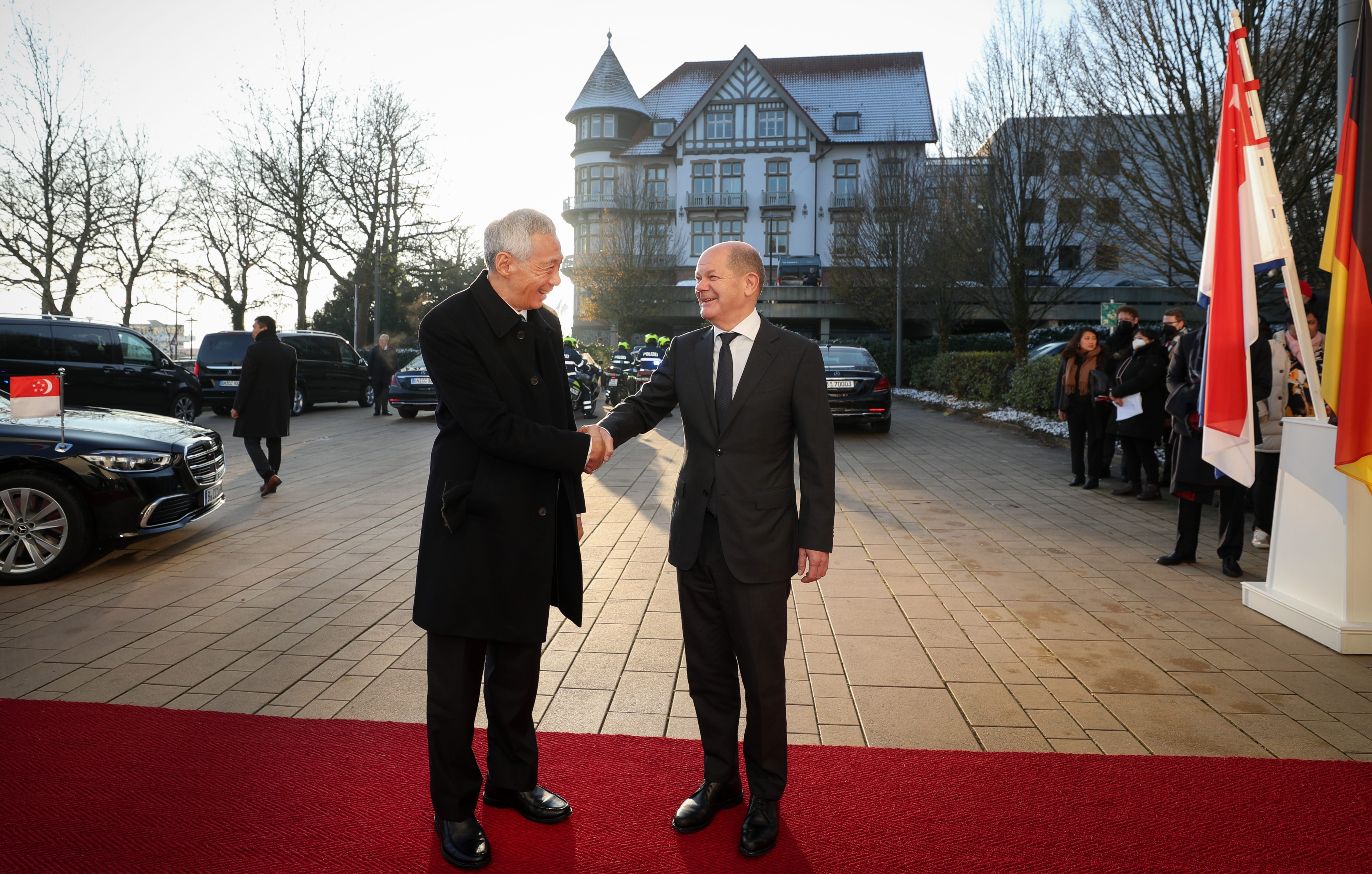 Lee Hsien Loong and Olaf Scholz in suits shake hands on a red carpet.