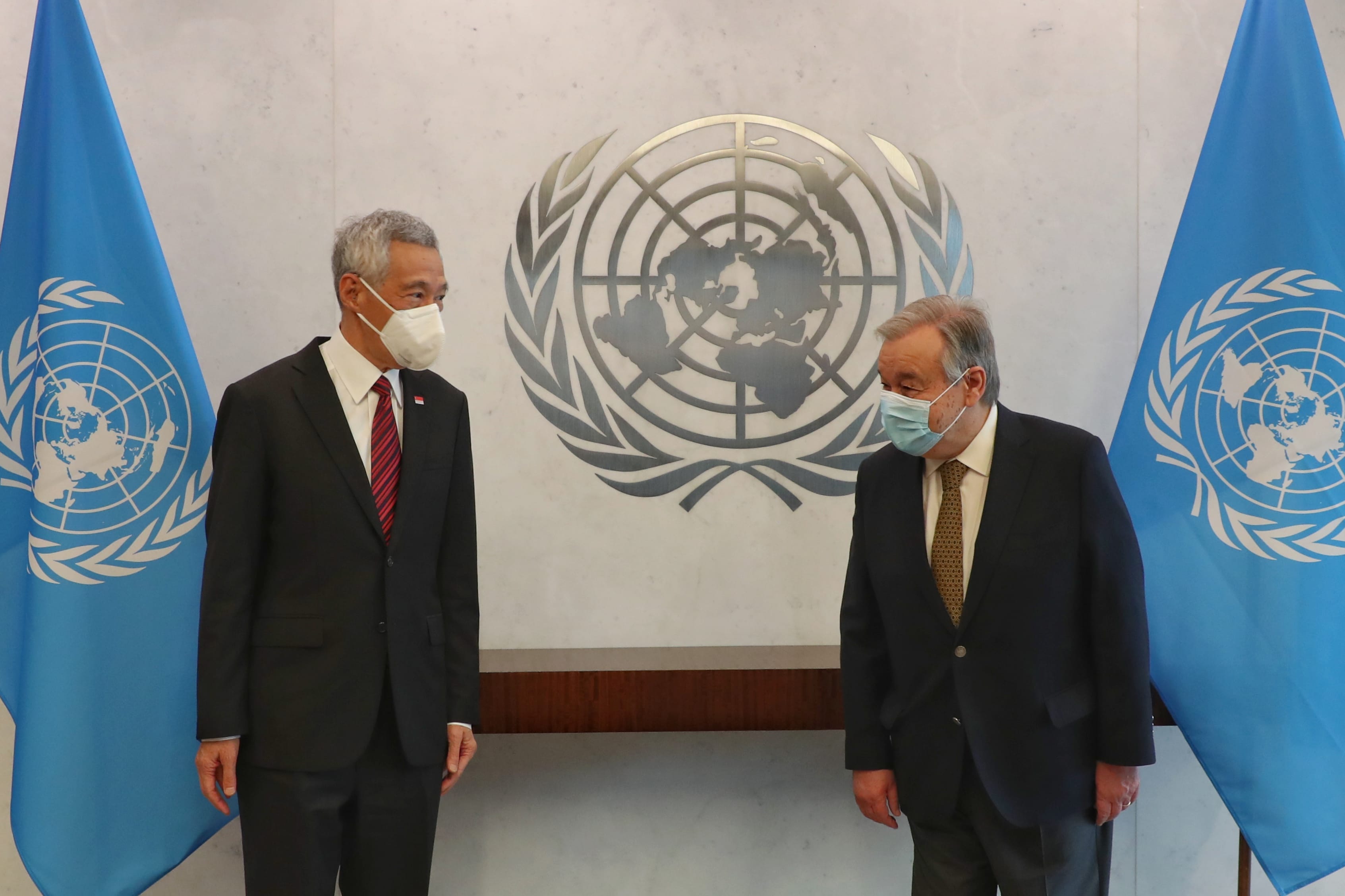 Lee Hsien Loong and António Guterres in suits, face masks, with UN flags and emblem.