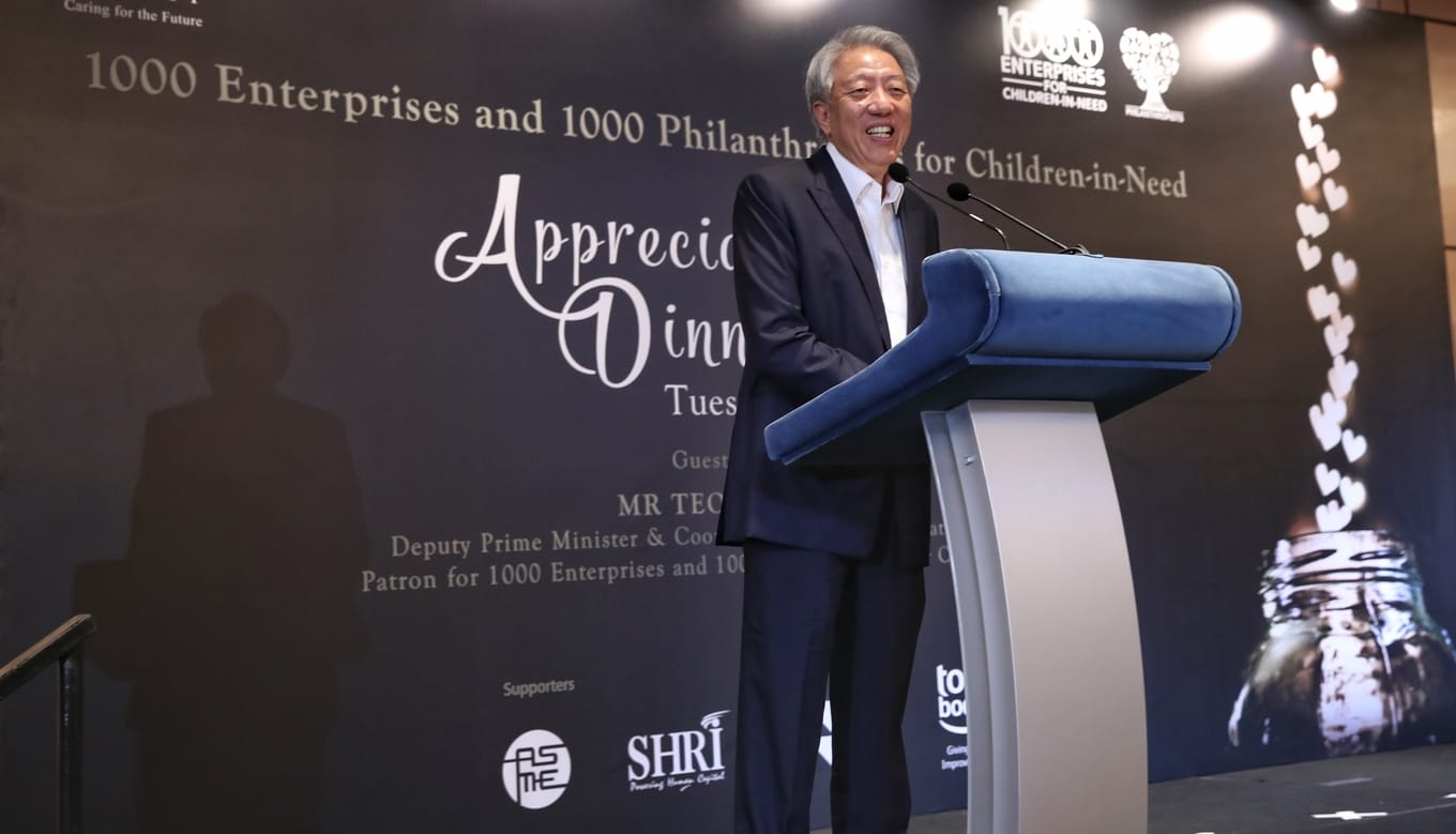 Man in suit at podium for "1000 Enterprises for Children-in-Need" event.
