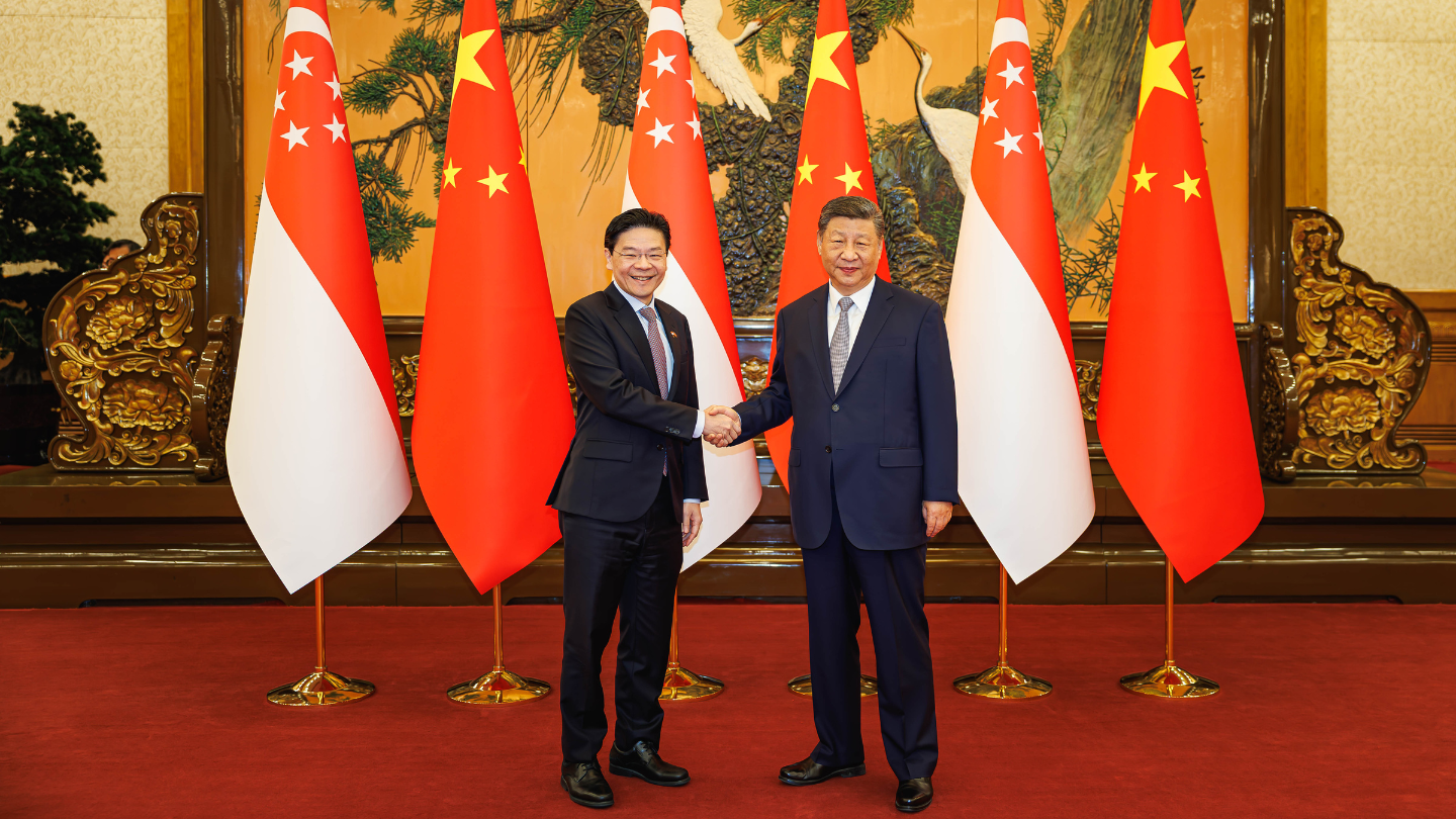 Two men in suits shake hands, with Singapore and China flags in the background.