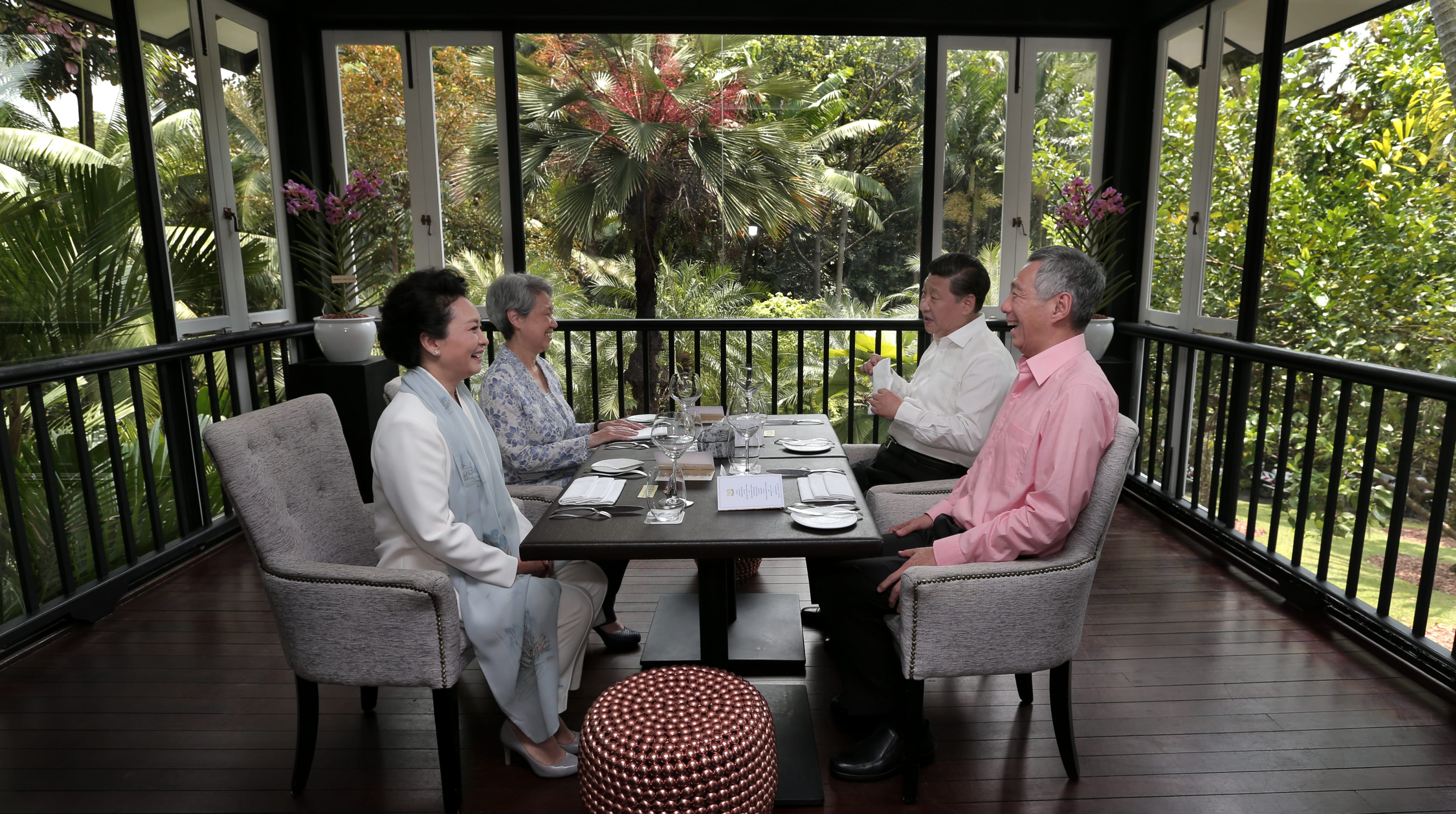 Xi Jinping and Lee Hsien Loong dining with their wives at a table overlooking lush greenery.