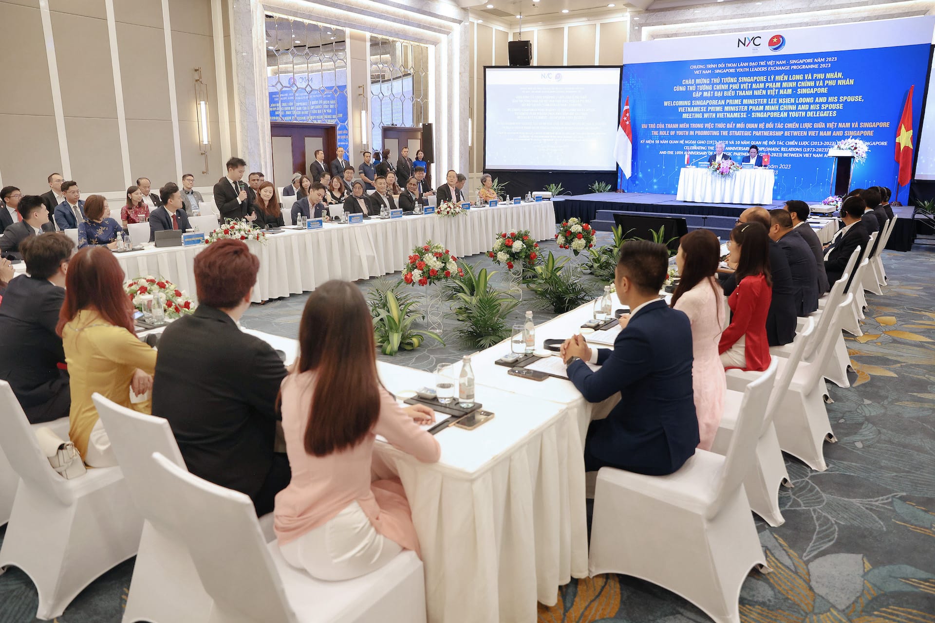Large meeting with seated people, long tables, a stage with text in Vietnamese and Singaporean flags.
