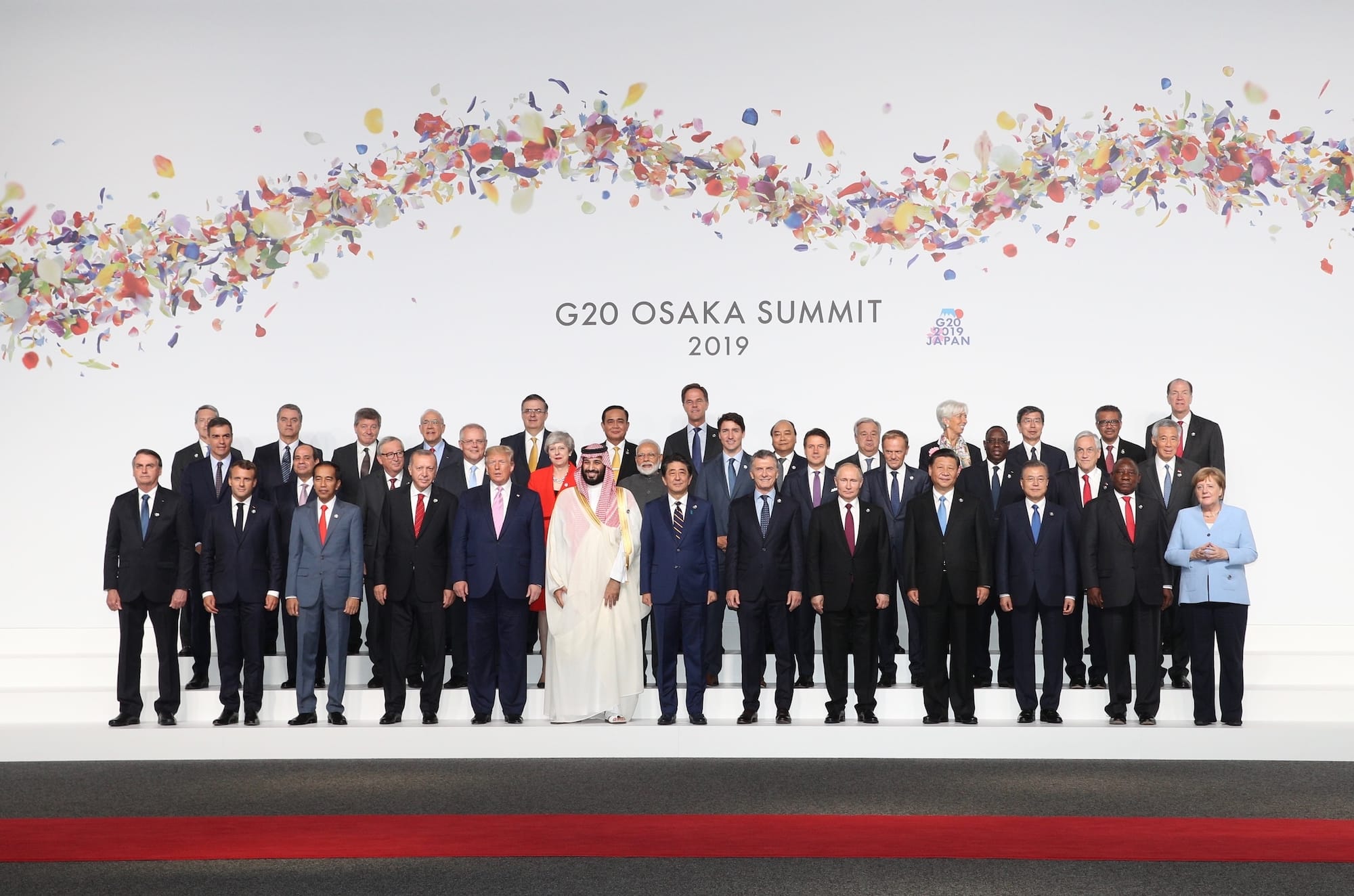 Group poses at G20 Osaka Summit 2019 against a backdrop of colorful paper confetti.