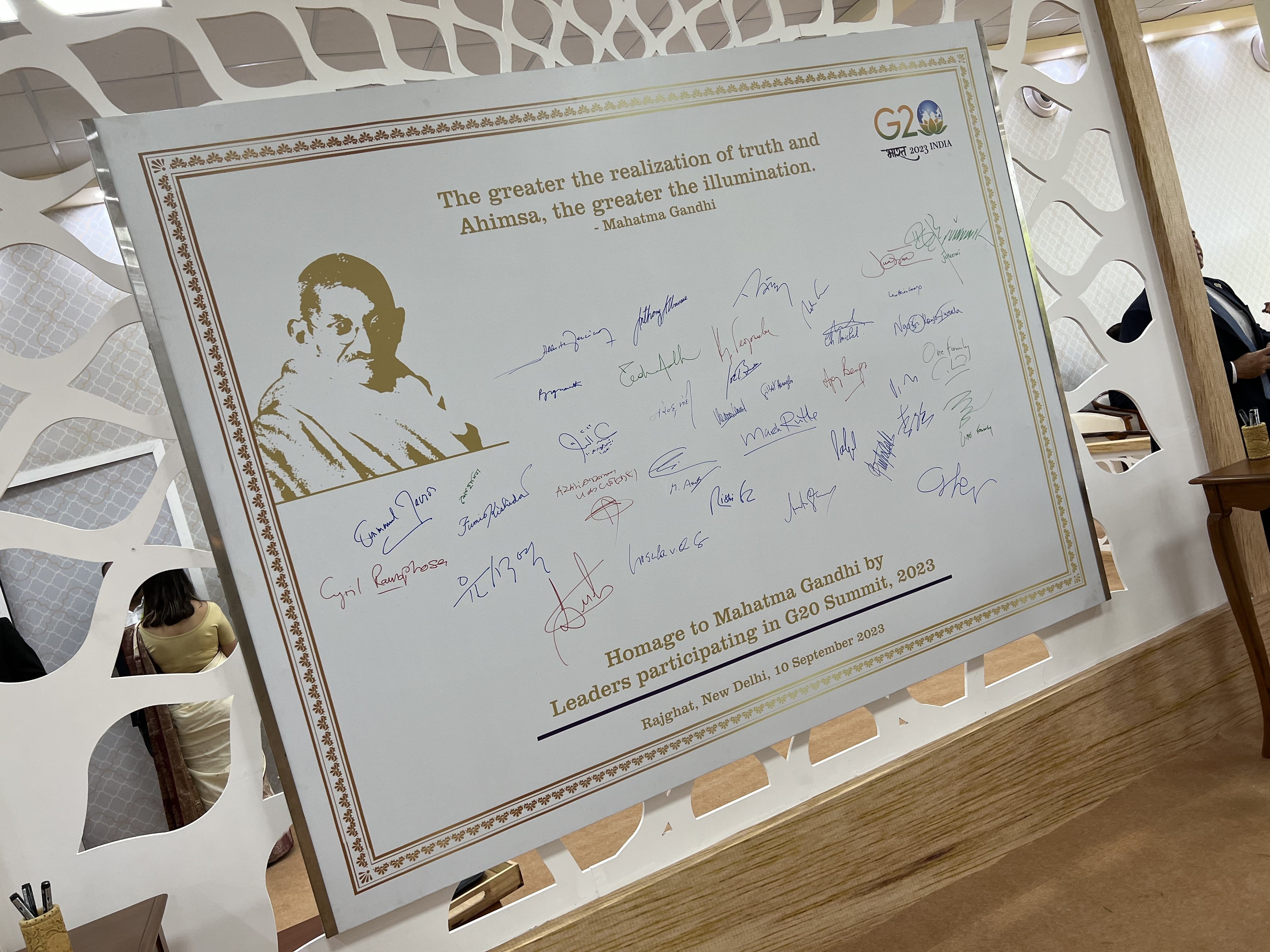 White board: Gandhi quote, portrait, G20 logo, signatures, & "Homage to Mahatma Gandhi by Leaders... G20 Summit, 2023."