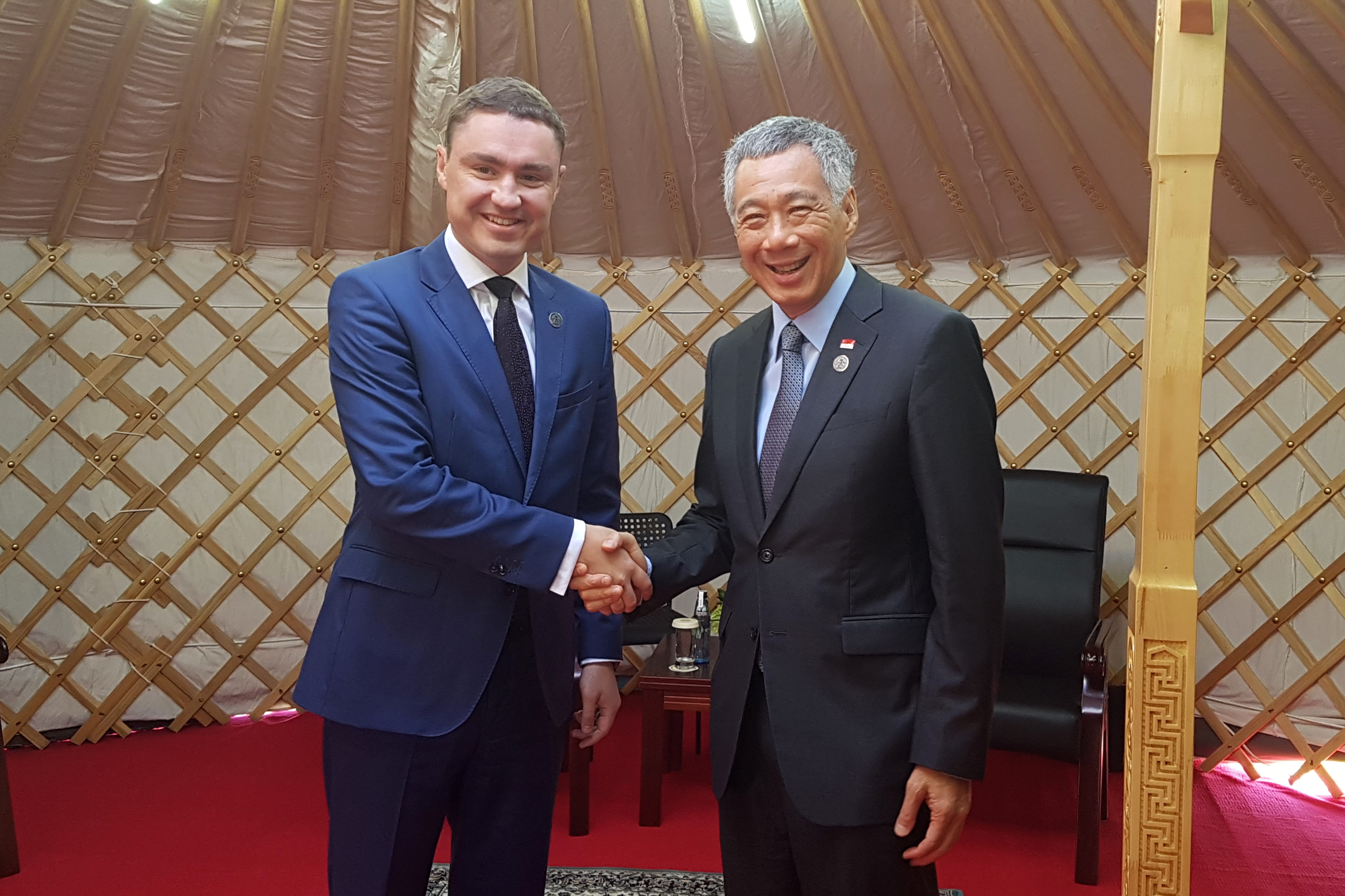 Two men in suits shaking hands, Lee Hsien Loong visible, inside a yurt.