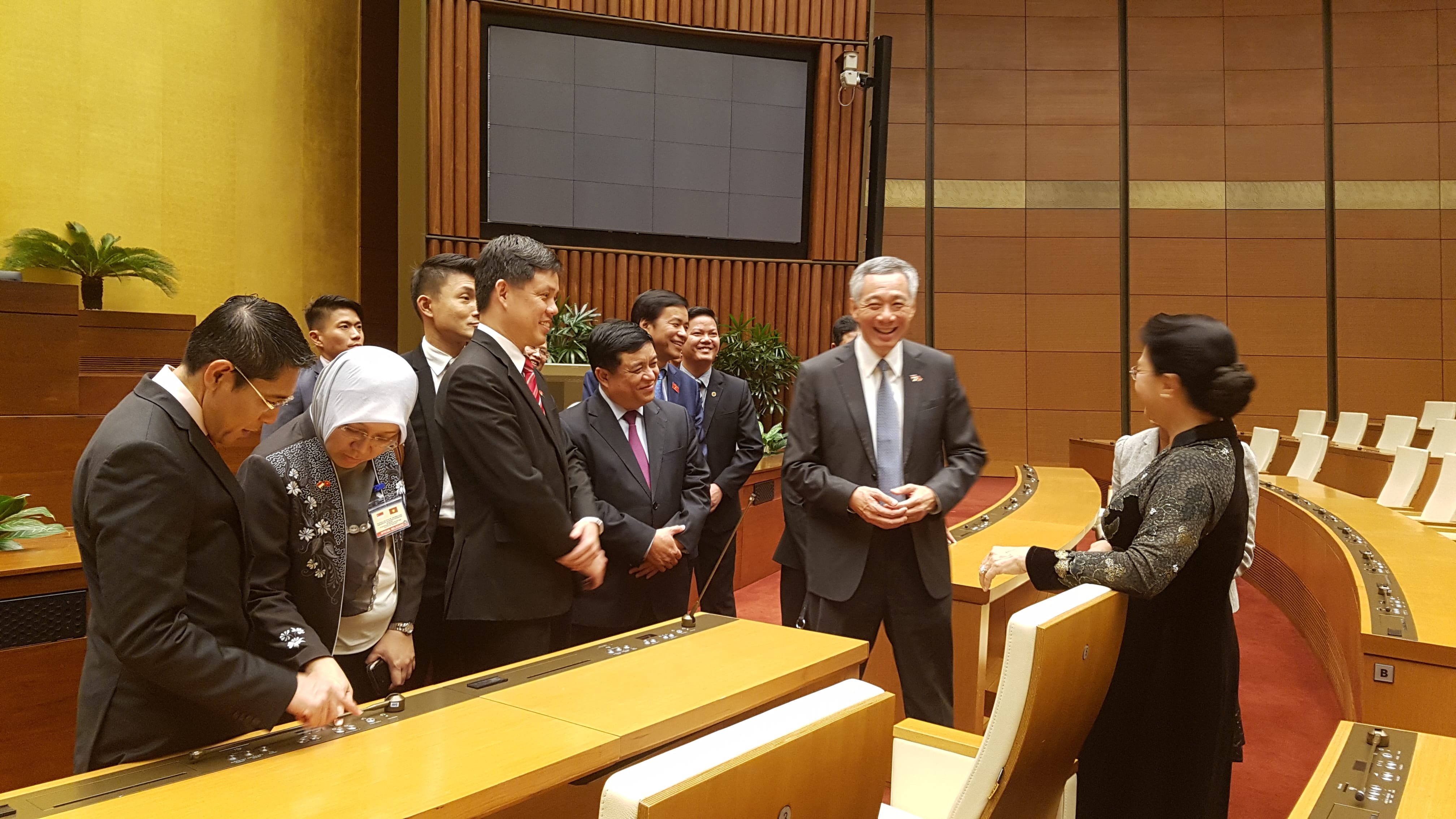 Lee Hsien Loong in a meeting with other officials in a wood-paneled room.