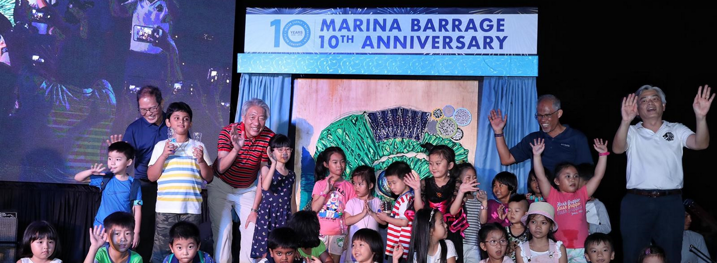 "Marina Barrage 10th Anniversary" event, group photo with adults and children waving.