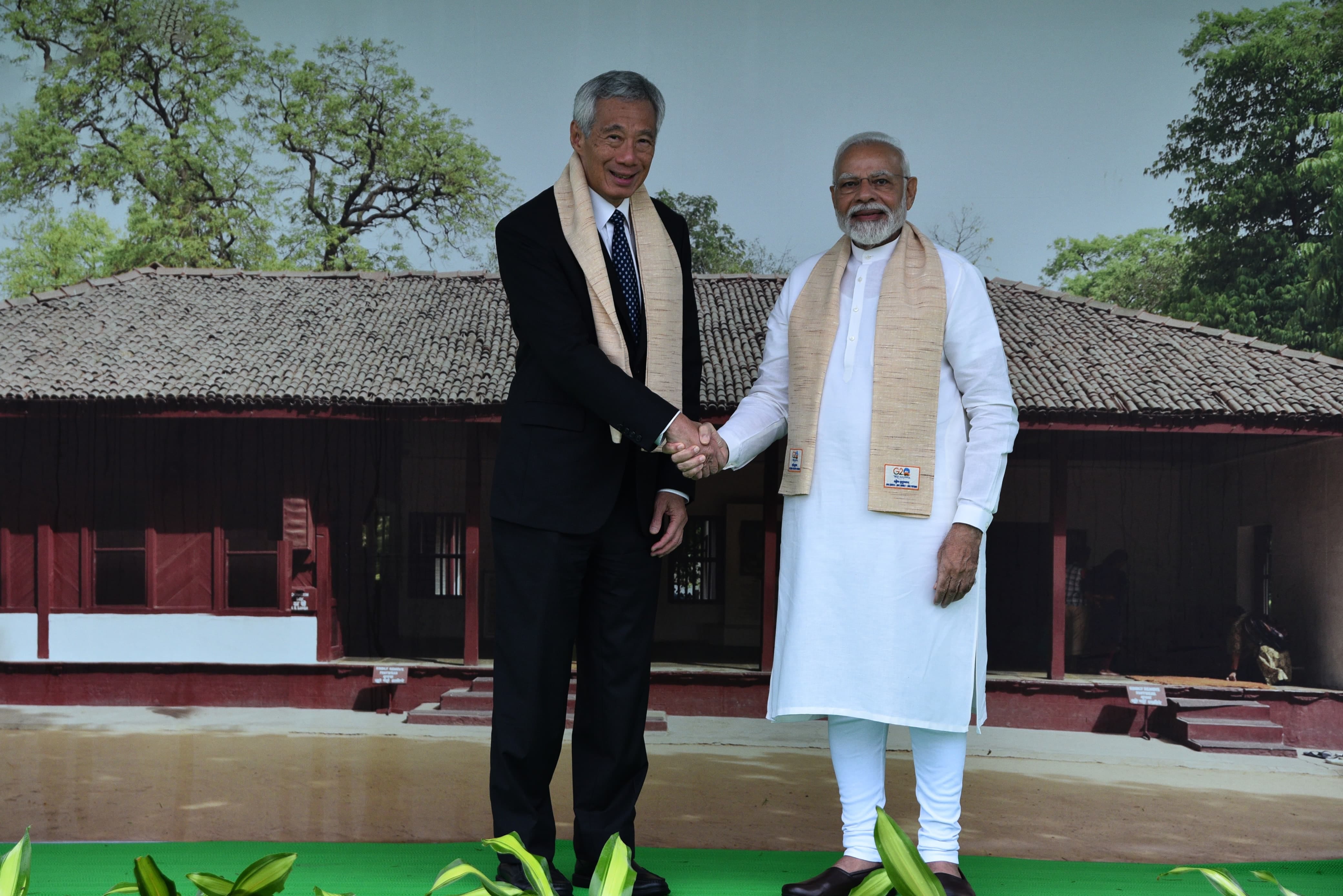 Lee Hsien Loong and Narendra Modi shake hands wearing scarves in front of a building image.