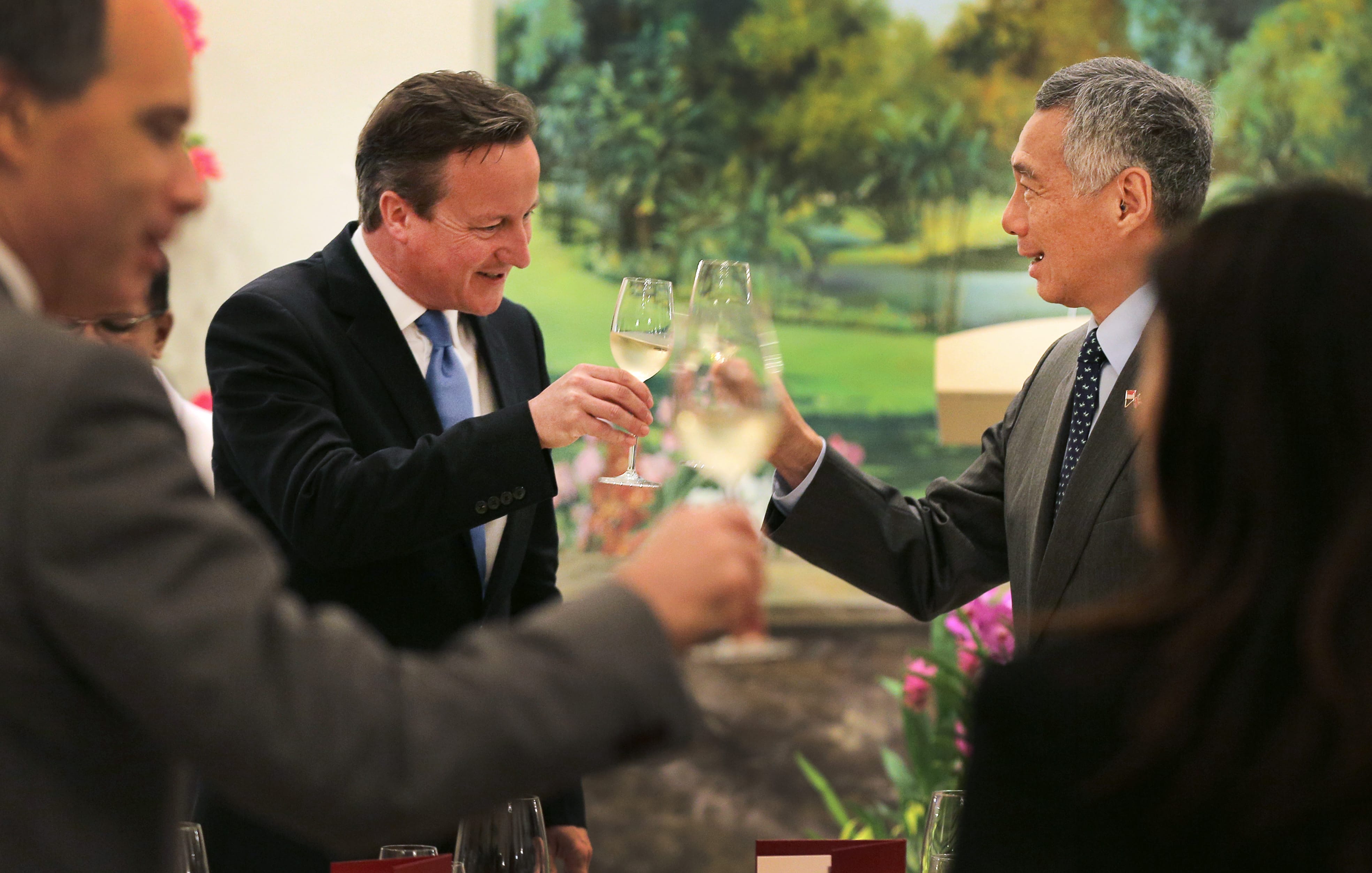 David Cameron and Lee Hsien Loong in suits, toasting with white wine glasses indoors.