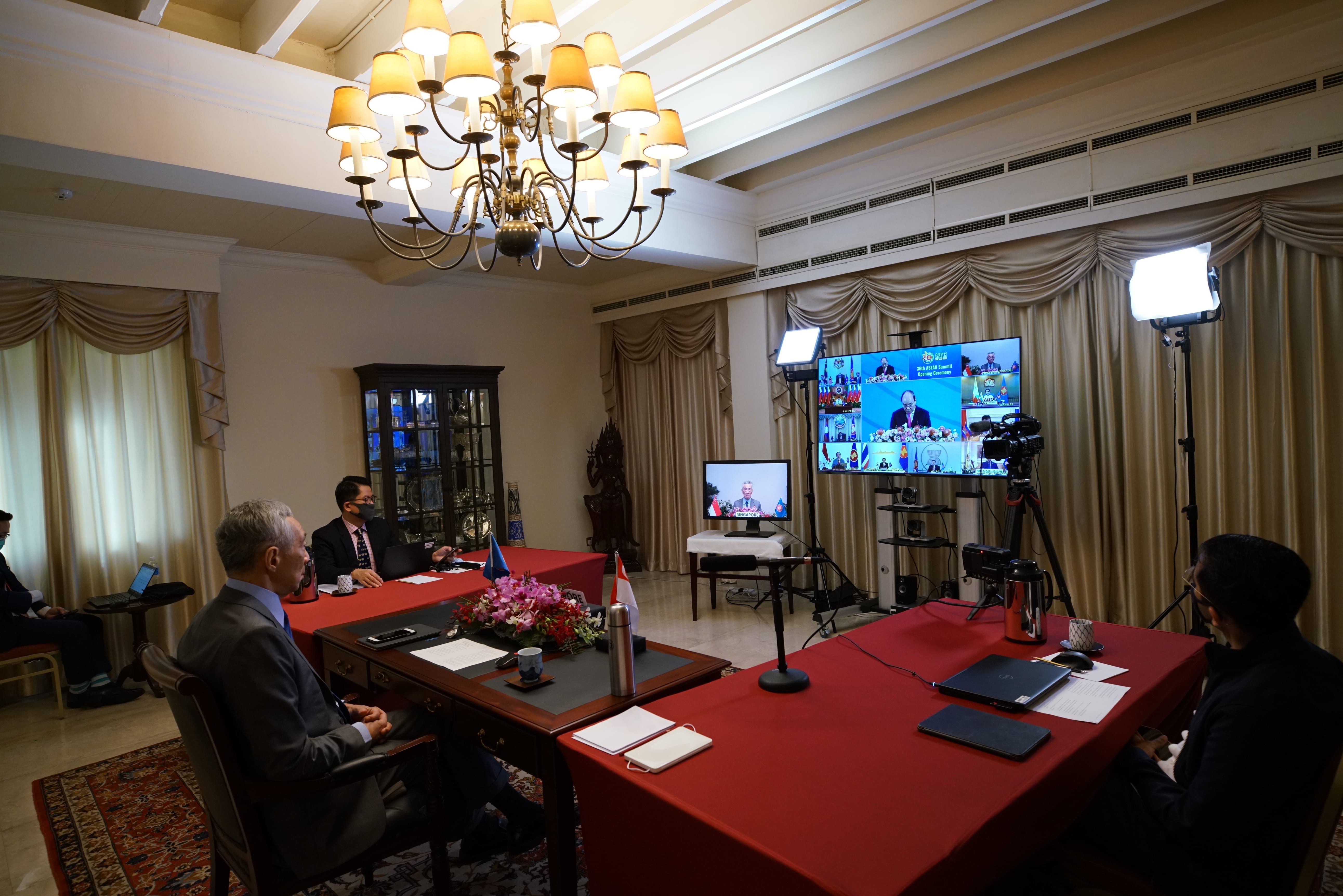People in room with monitors showing a video conference, and camera equipment present.