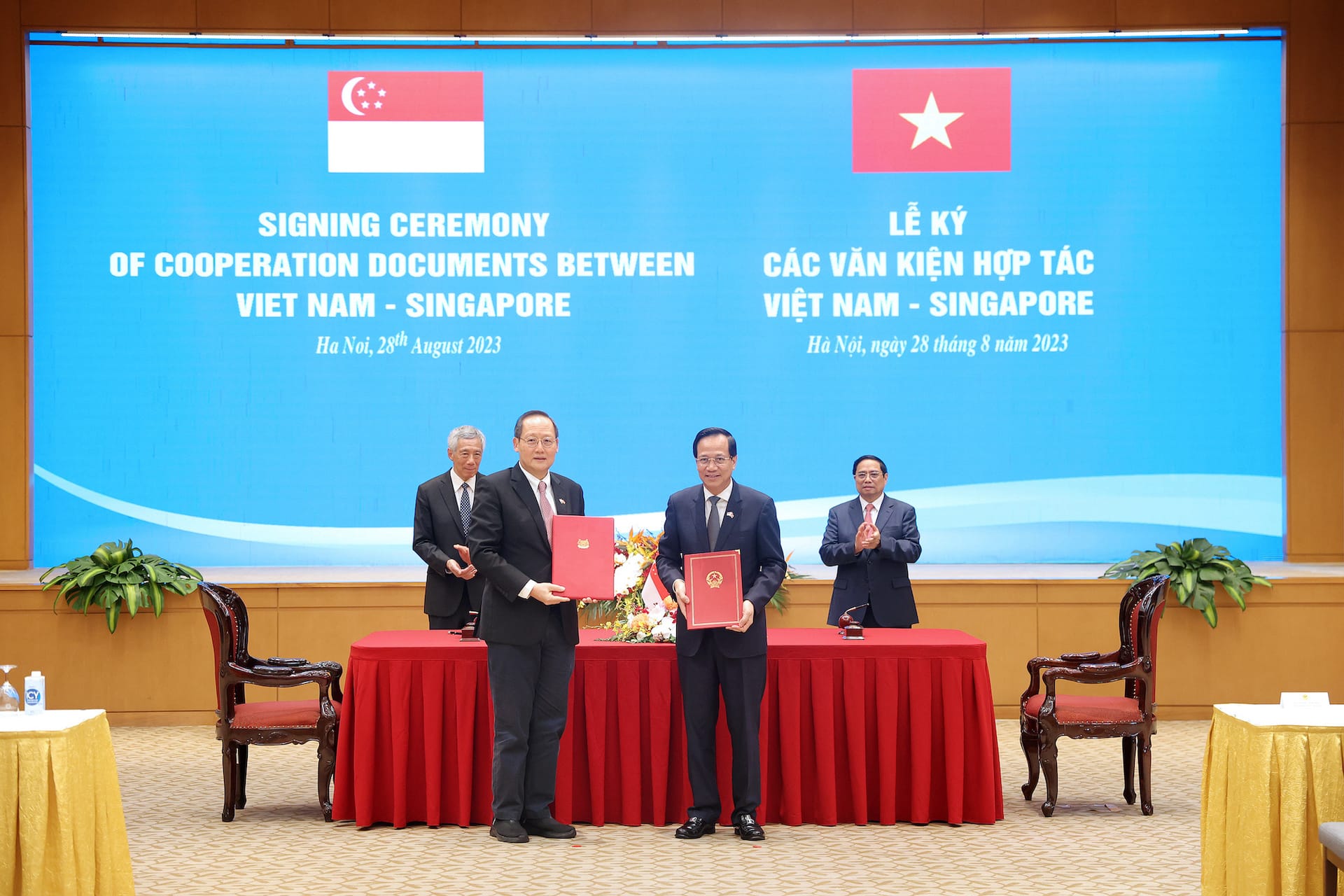 Signing ceremony with Vietnam, Singapore flags; men holding documents, others clapping.