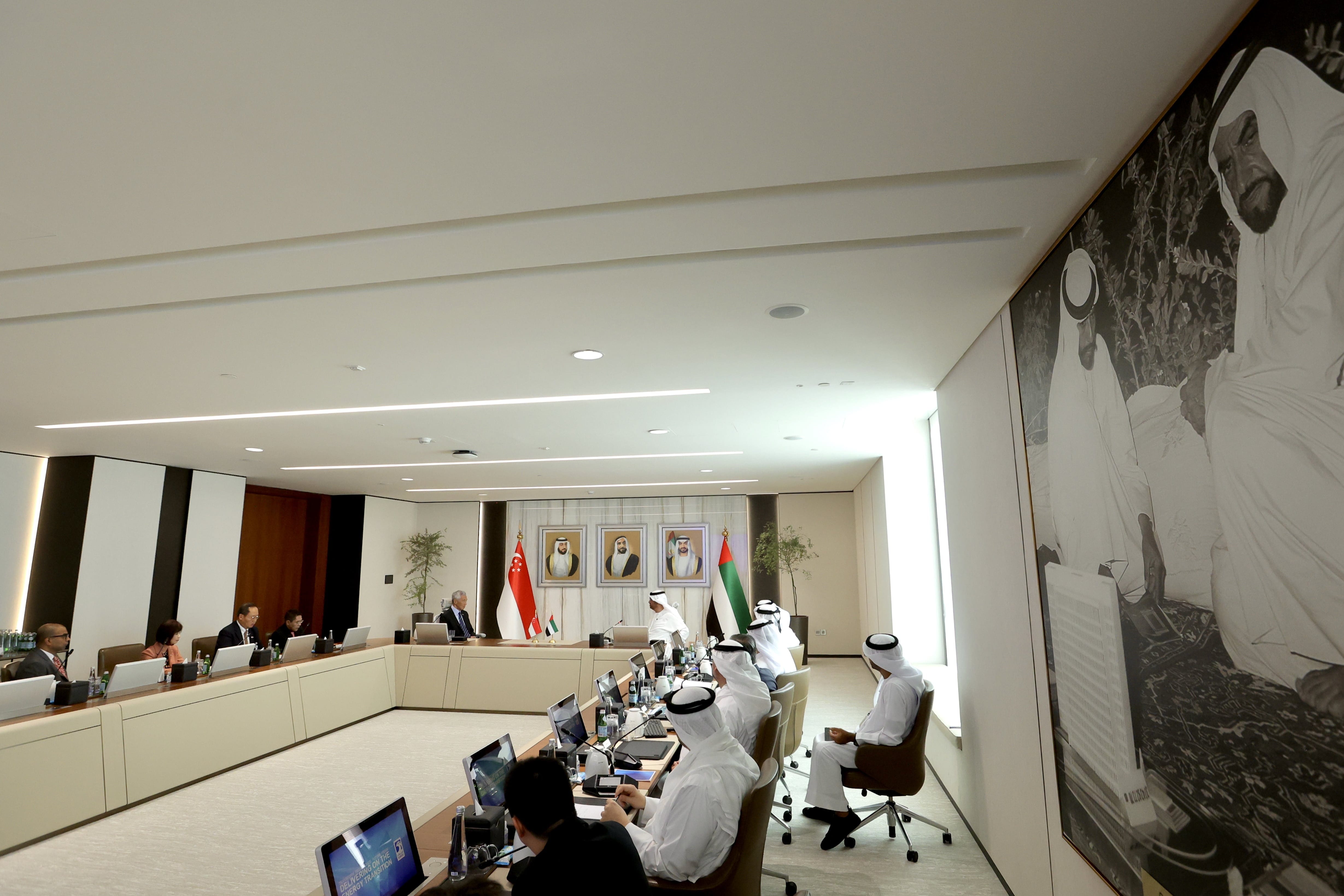 Meeting room with participants, flags of Singapore and UAE, portraits, and large wall art.