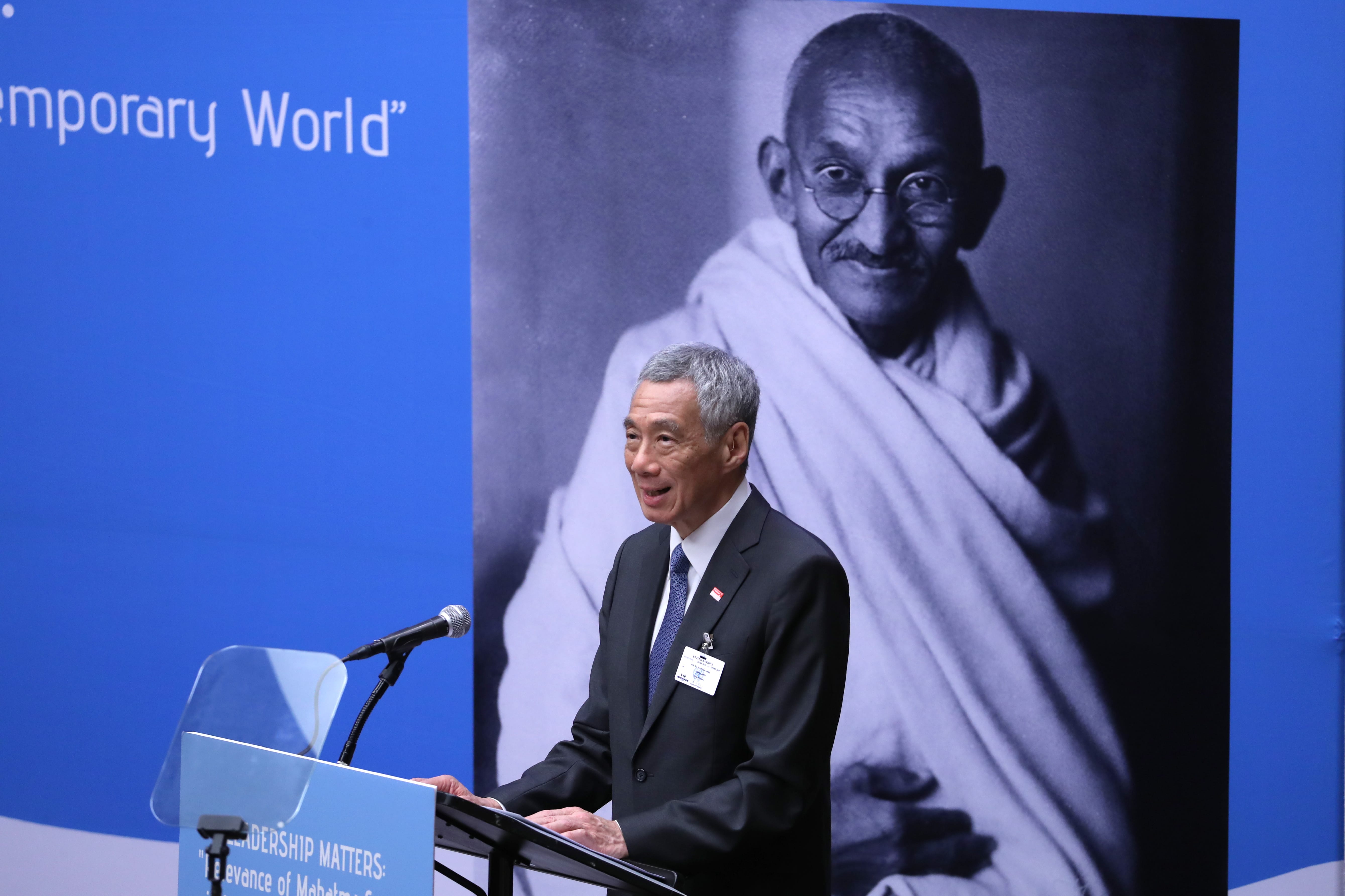 Lee Hsien Loong at podium, Mahatma Gandhi's portrait backdrop.