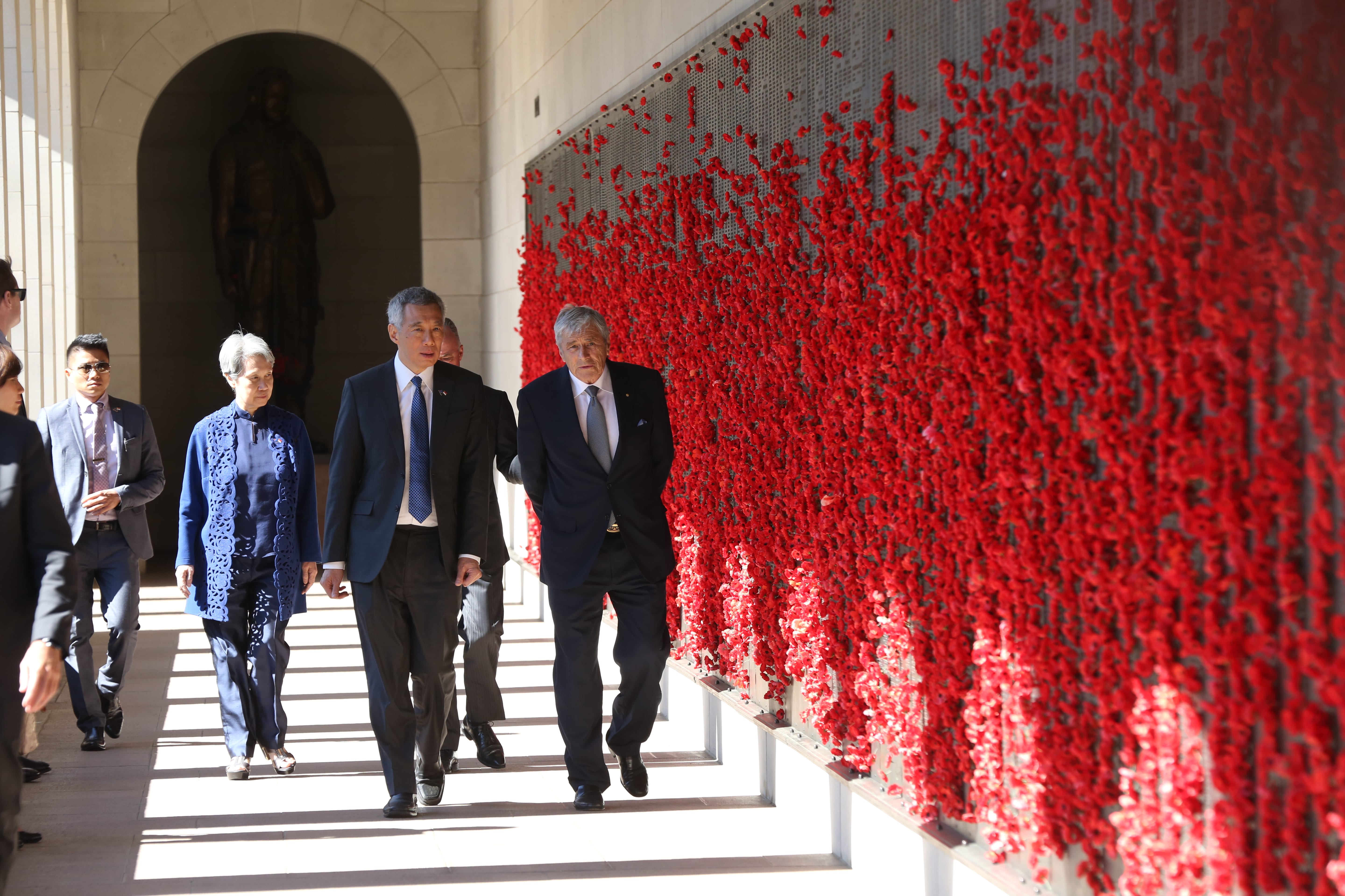 Lee Hsien Loong and John Howard walk past a wall covered in red poppies.