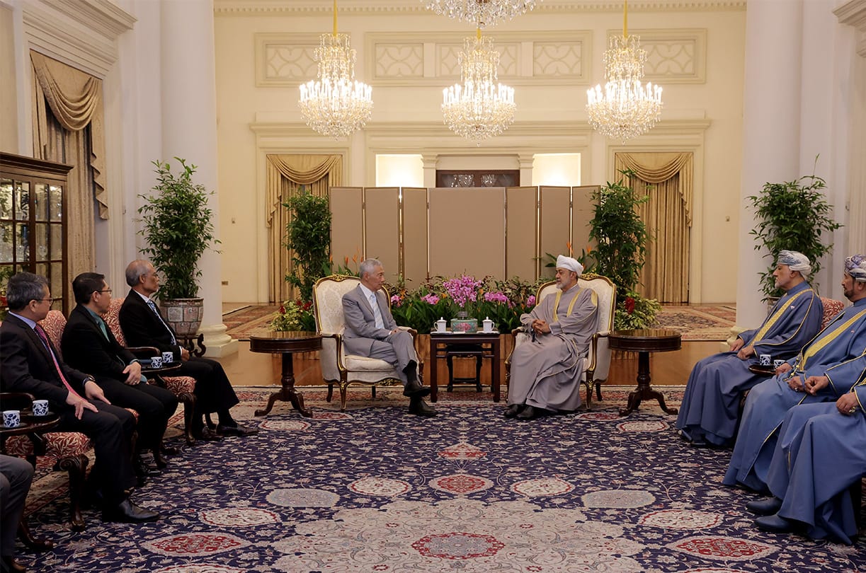 Group of men meeting, seated in chairs on a patterned rug in a large room.